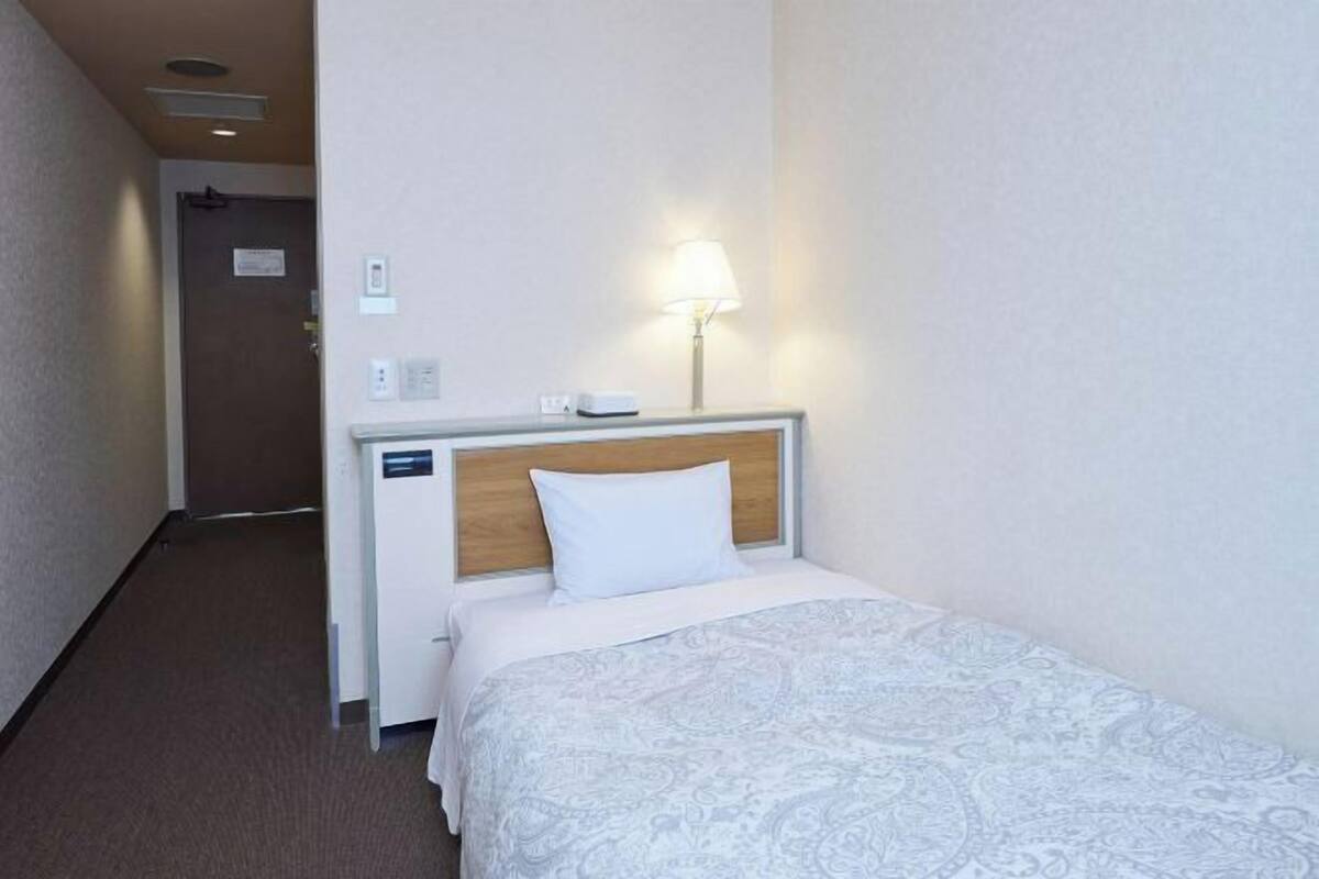 A hotel room with a bed, a bedside table, a lamp, and a wall-mounted phone.