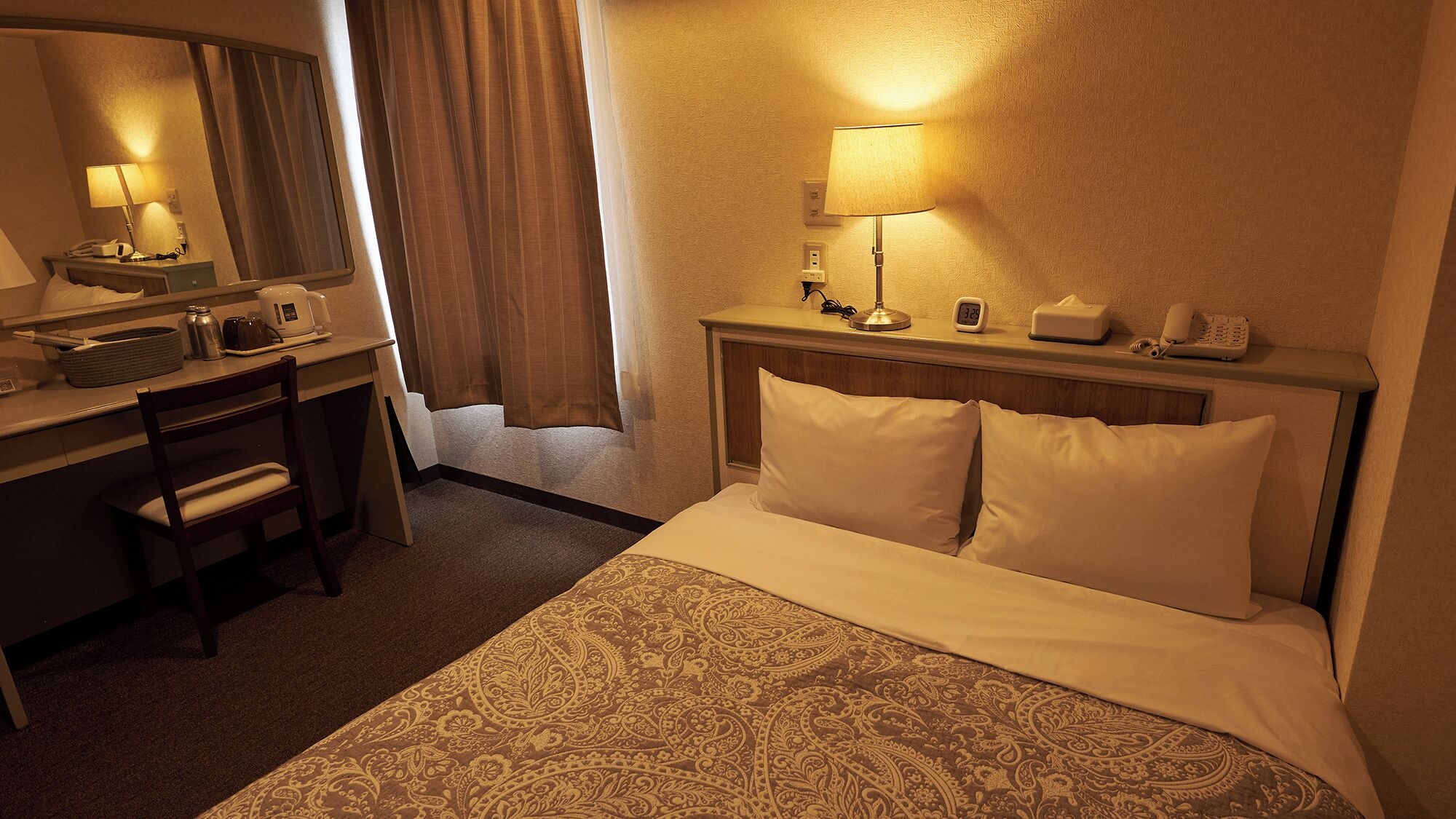 Een hotelkamer met een bed, een bureau met een lamp, een telefoon en een klok.