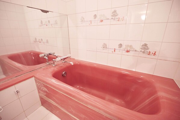 A bathroom with a red bathtub, a mirror, and white tiled walls with decorative tiles.