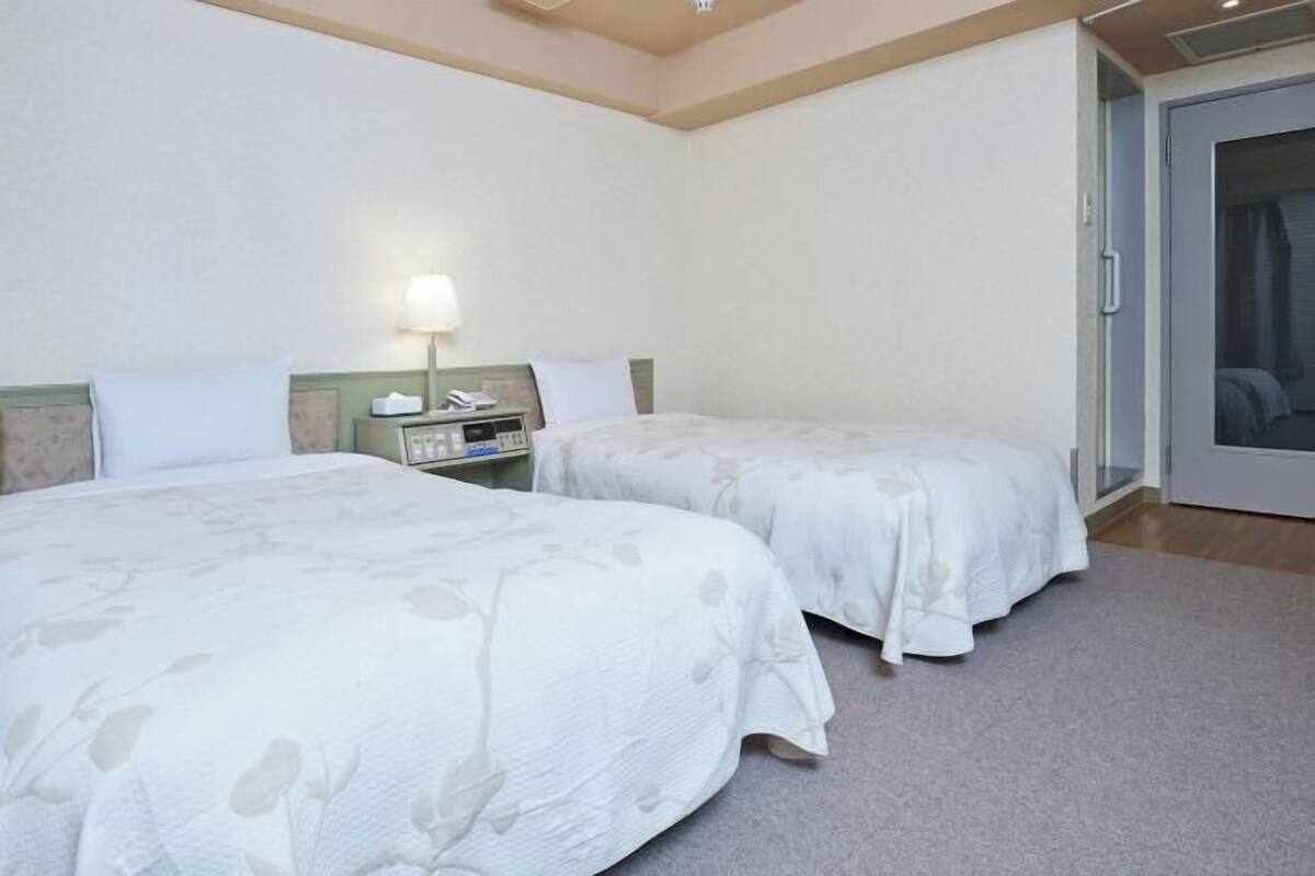 A hotel room with two beds, a nightstand, a lamp, and a sliding door to a balcony.