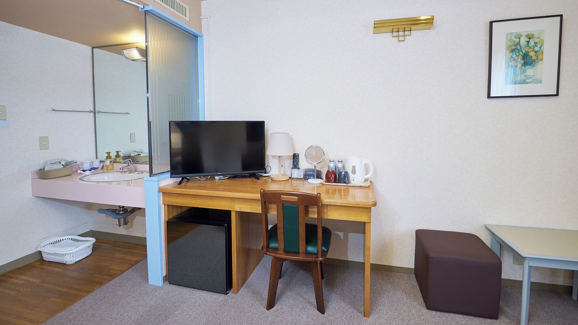 A hotel room with a wooden desk, a television, a mirror, a small table, and a chair.