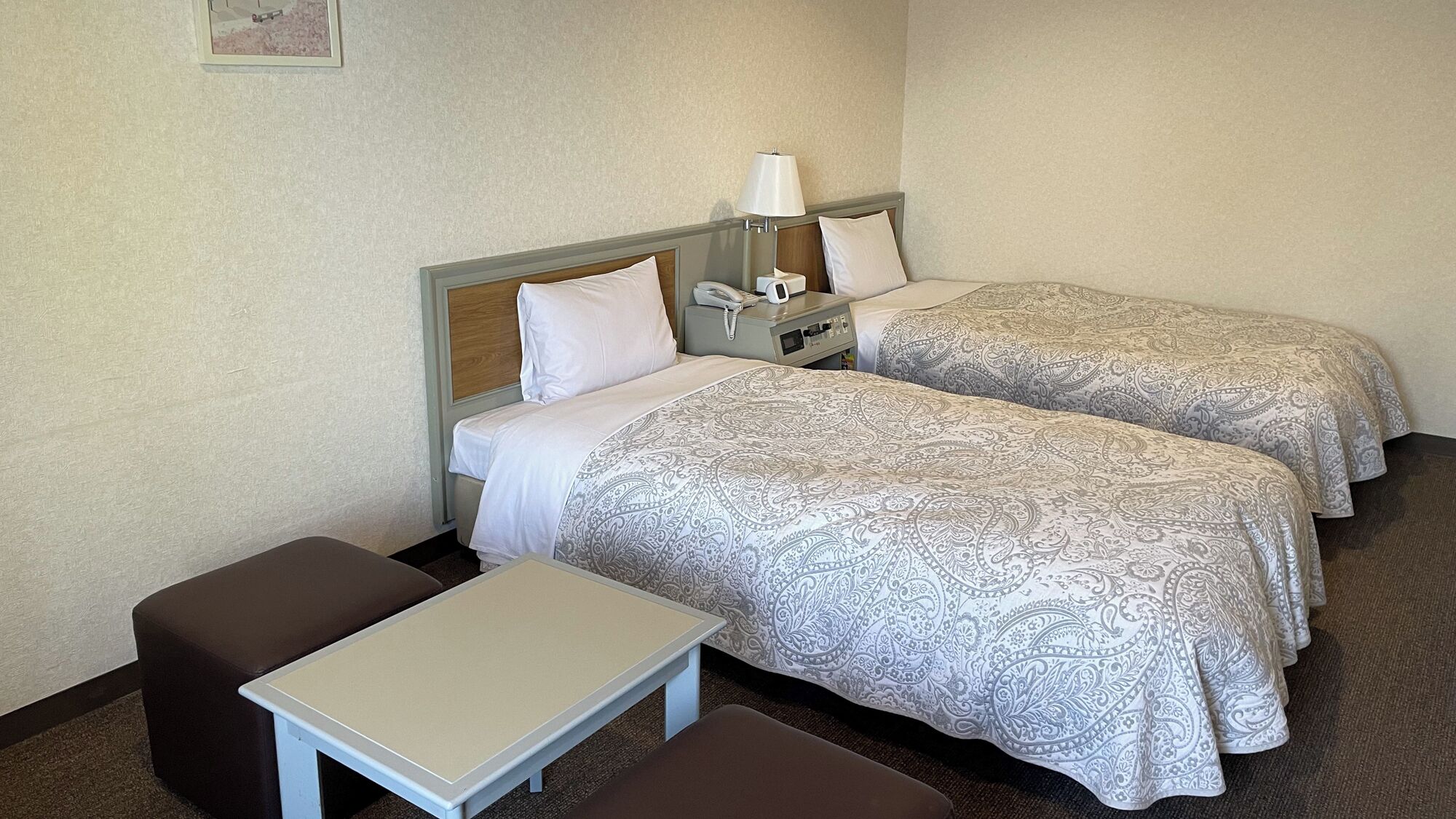 A hotel room with two beds, a bedside table, a lamp, and a telephone.
