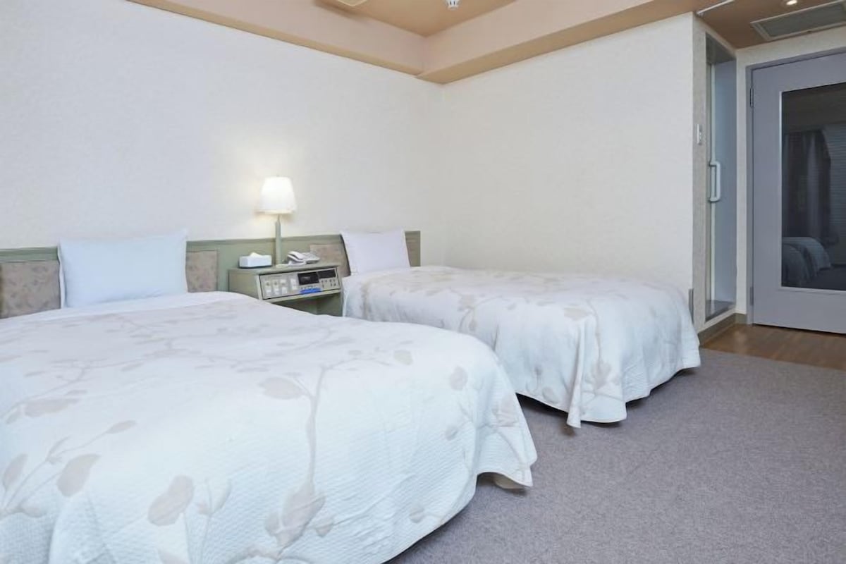 A hotel room with two beds, a nightstand, a lamp, and a sliding door to a balcony.