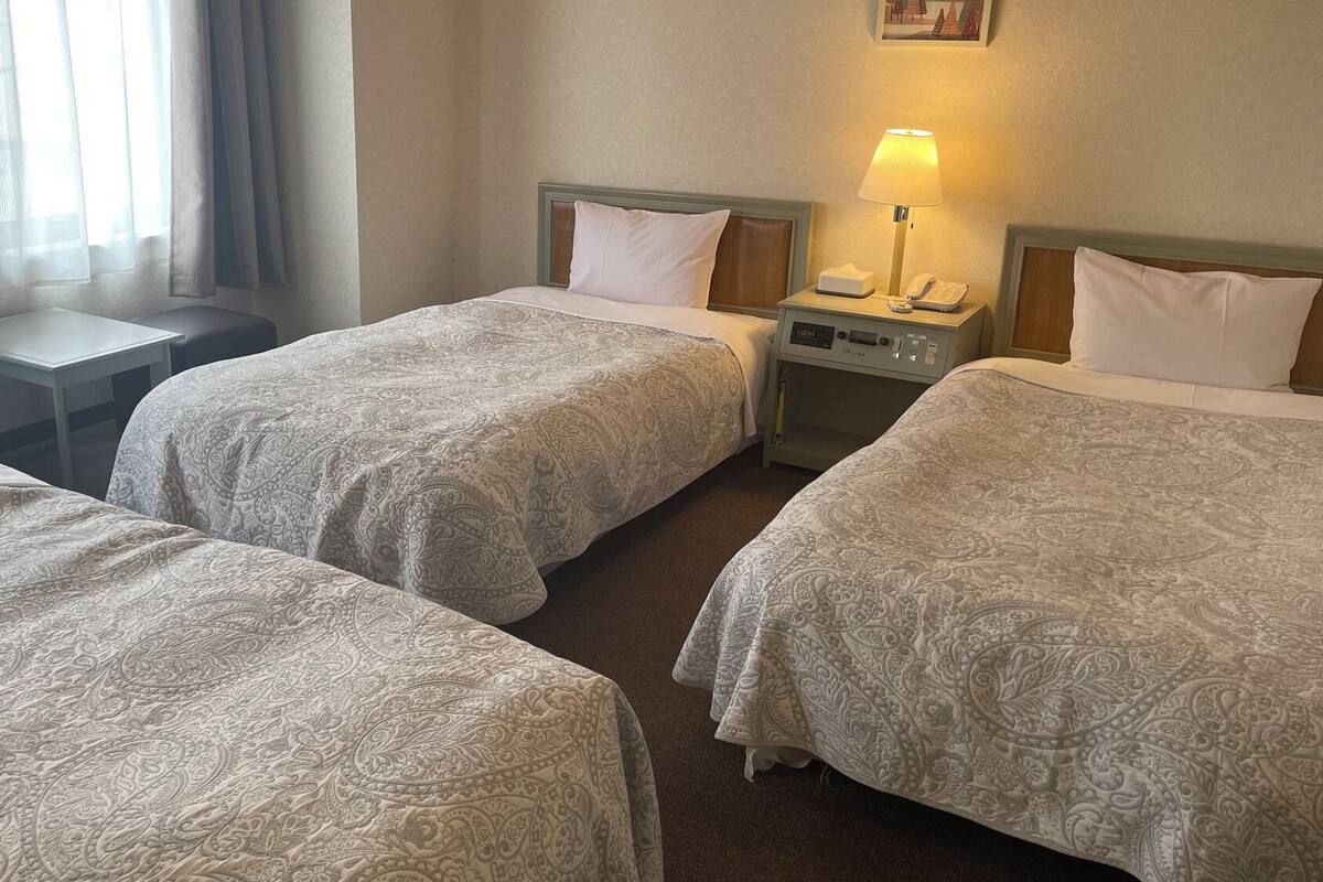 A hotel room with three beds, a desk, a lamp, and a telephone.