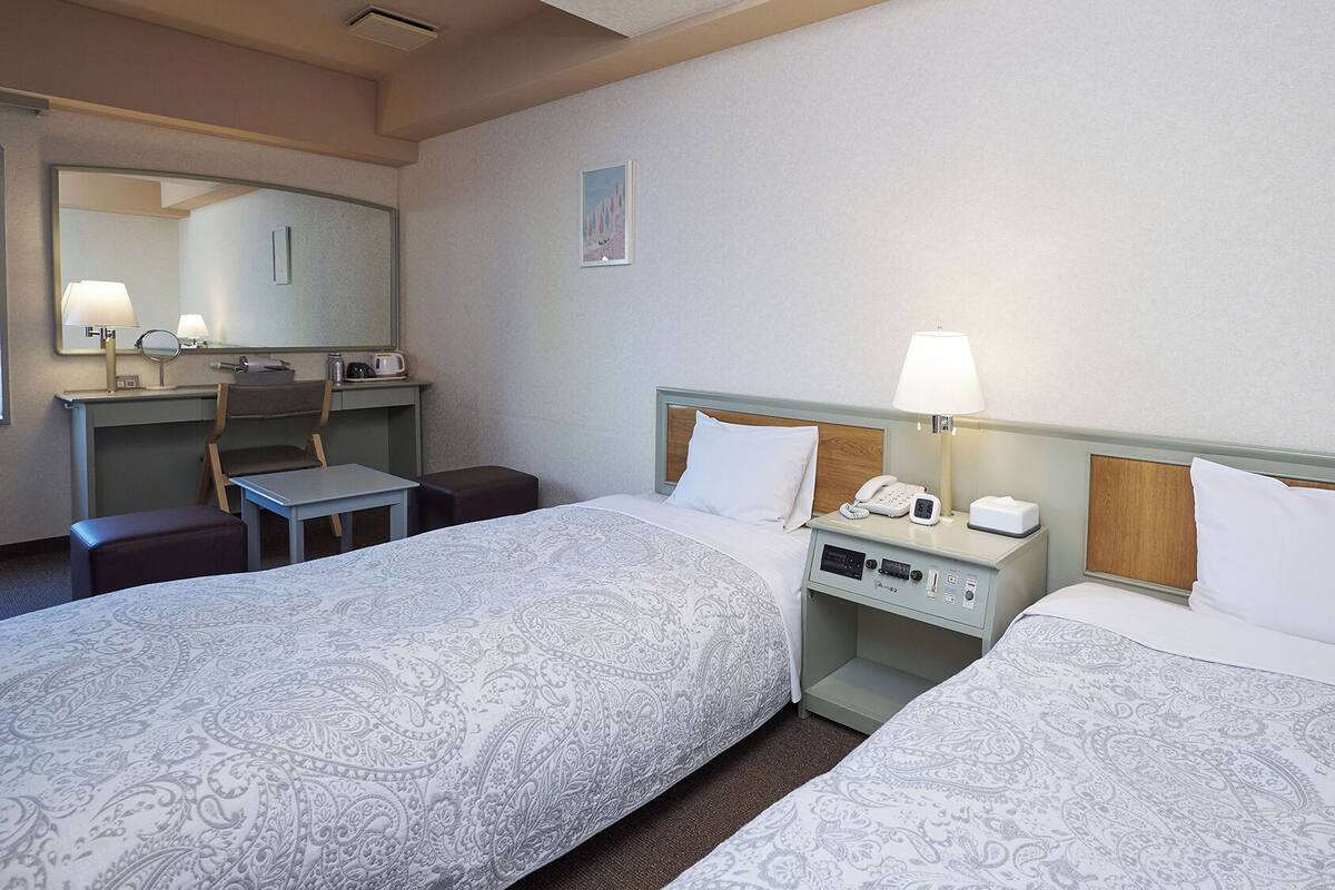 A hotel room with two beds, a desk, a chair, a telephone, and a mirror.