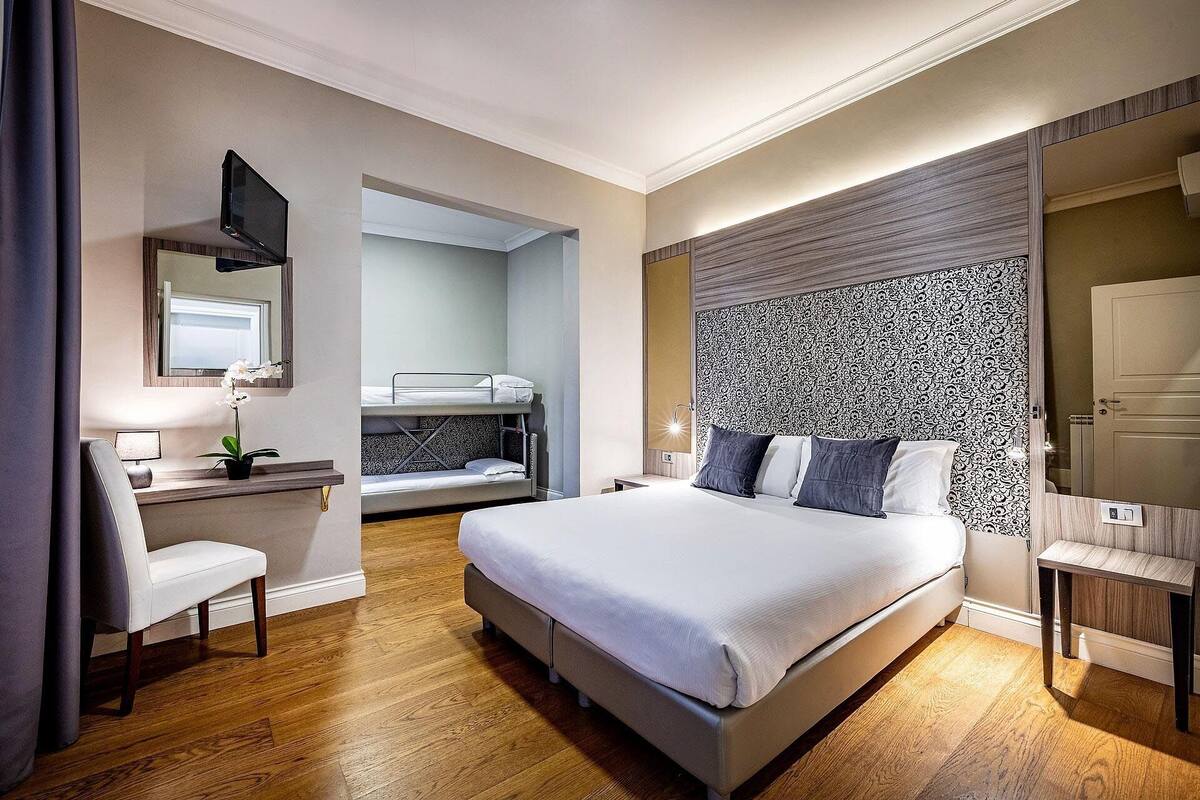 A hotel room with a large bed, a desk with a chair, a television, and a bathroom visible through an open door.