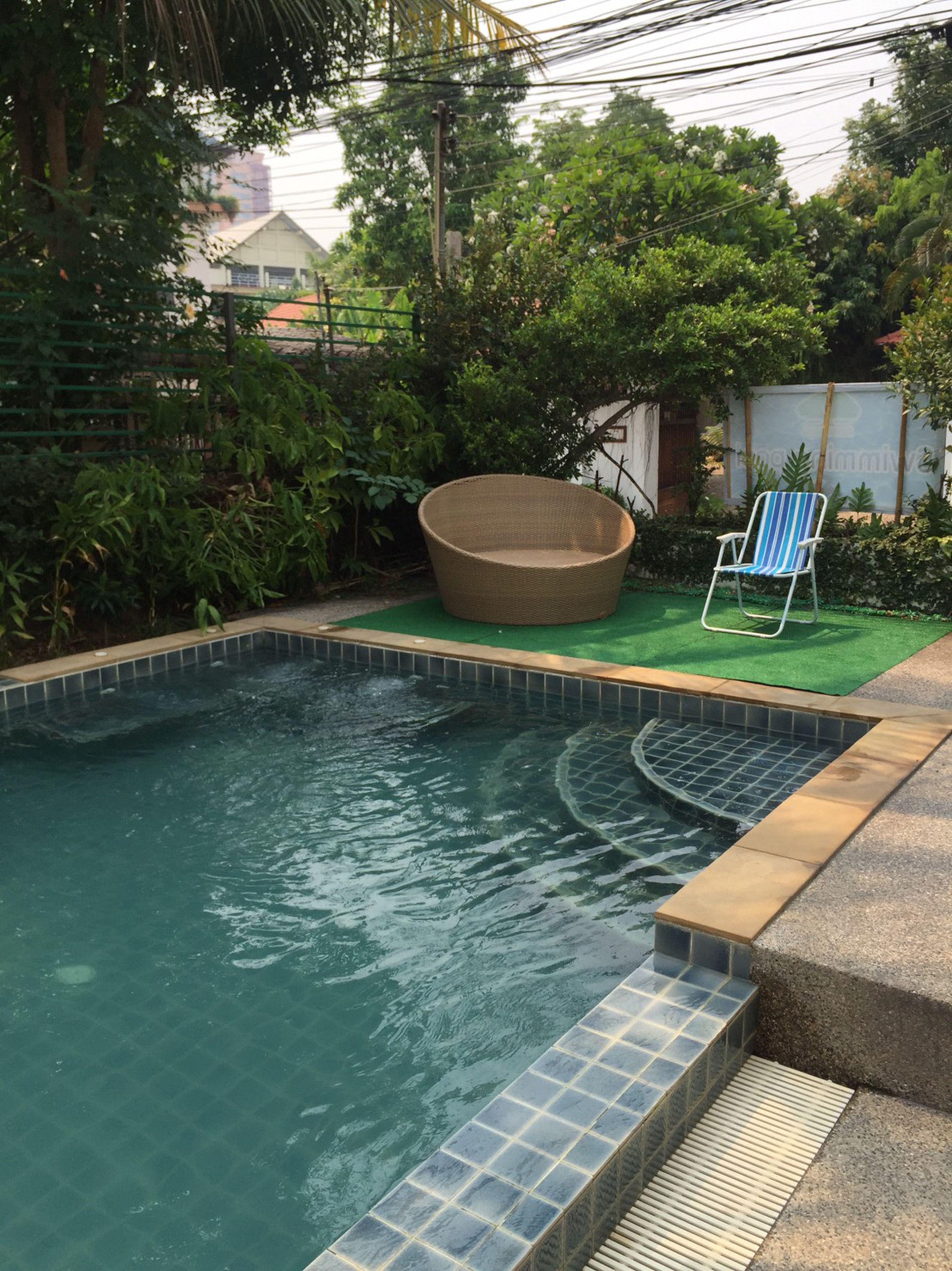 A swimming pool with a tiled edge, a wicker chair, and a striped lounge chair.