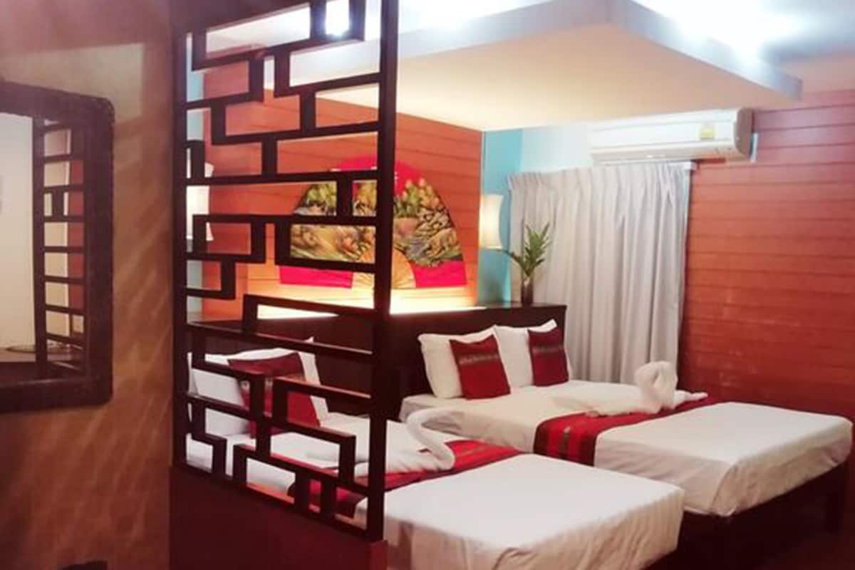 A hotel room with two beds, a decorative partition, a ceiling fan, and a wall-mounted air conditioner.