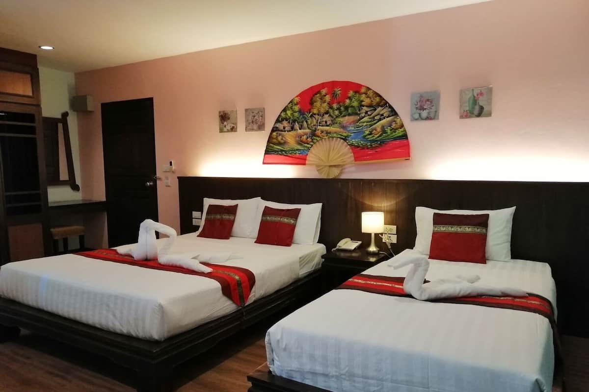 A hotel room with two beds, each with white linens and red pillows, a large decorative wall hanging above the beds, and a wooden headboard.