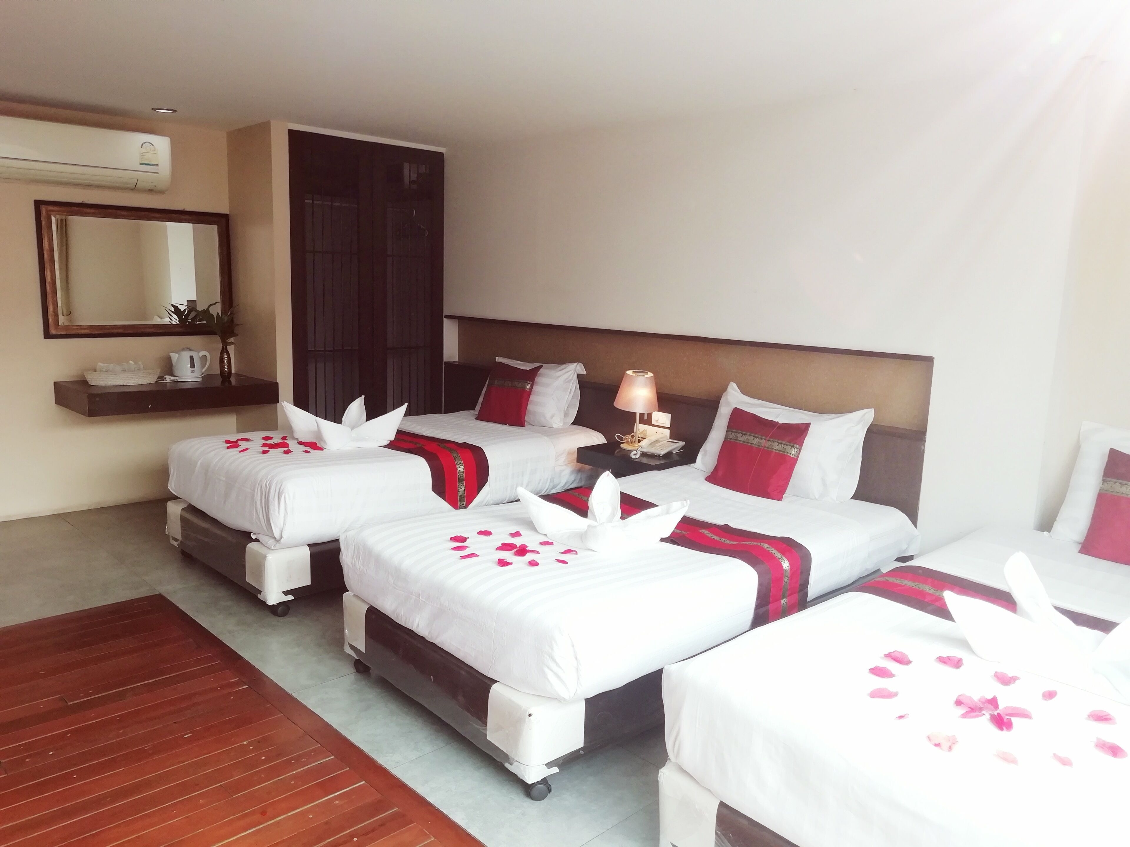 A hotel room with four beds, a bedside table with a lamp, a mirror, and a wall-mounted air conditioner.