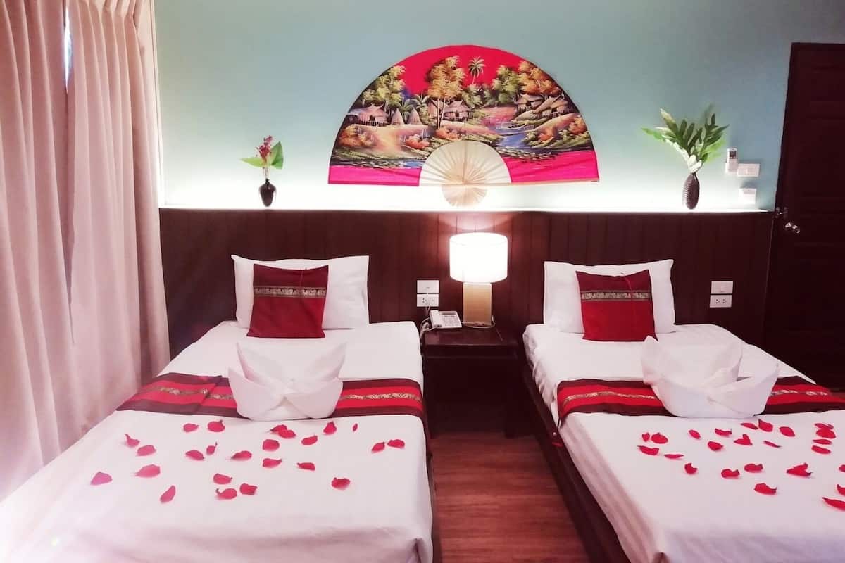 A hotel room with two beds, a nightstand with a lamp, a wall-mounted painting, and a potted plant.