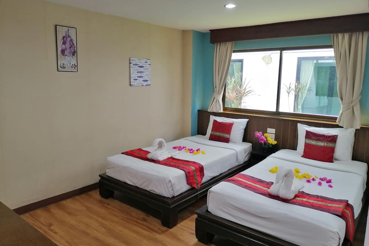 A hotel room with two beds, wooden headboards, white bedding, red and gold decorative pillows, and a window with curtains.