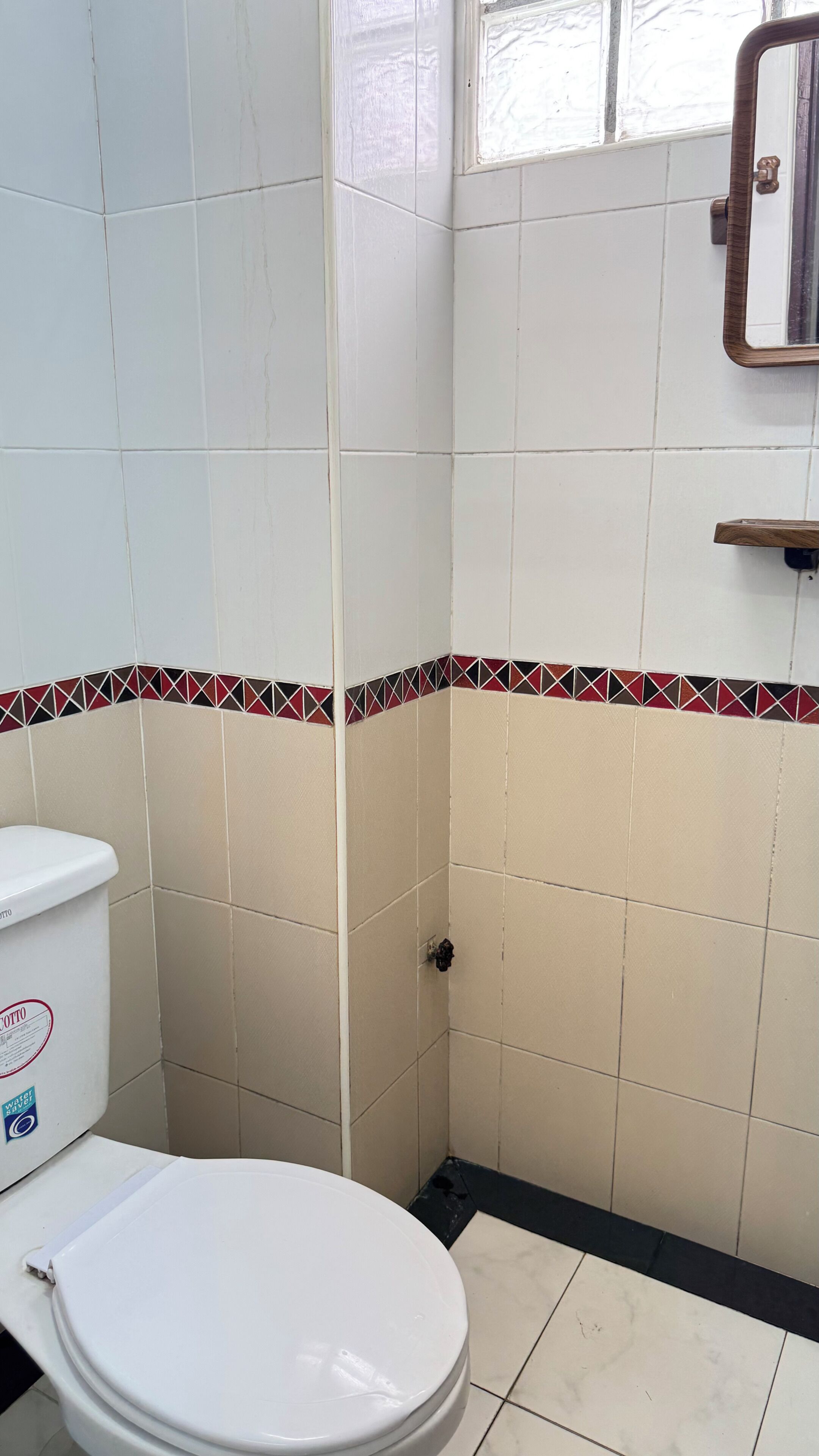 A bathroom with white tiles, a toilet, a shower, and a mirror.