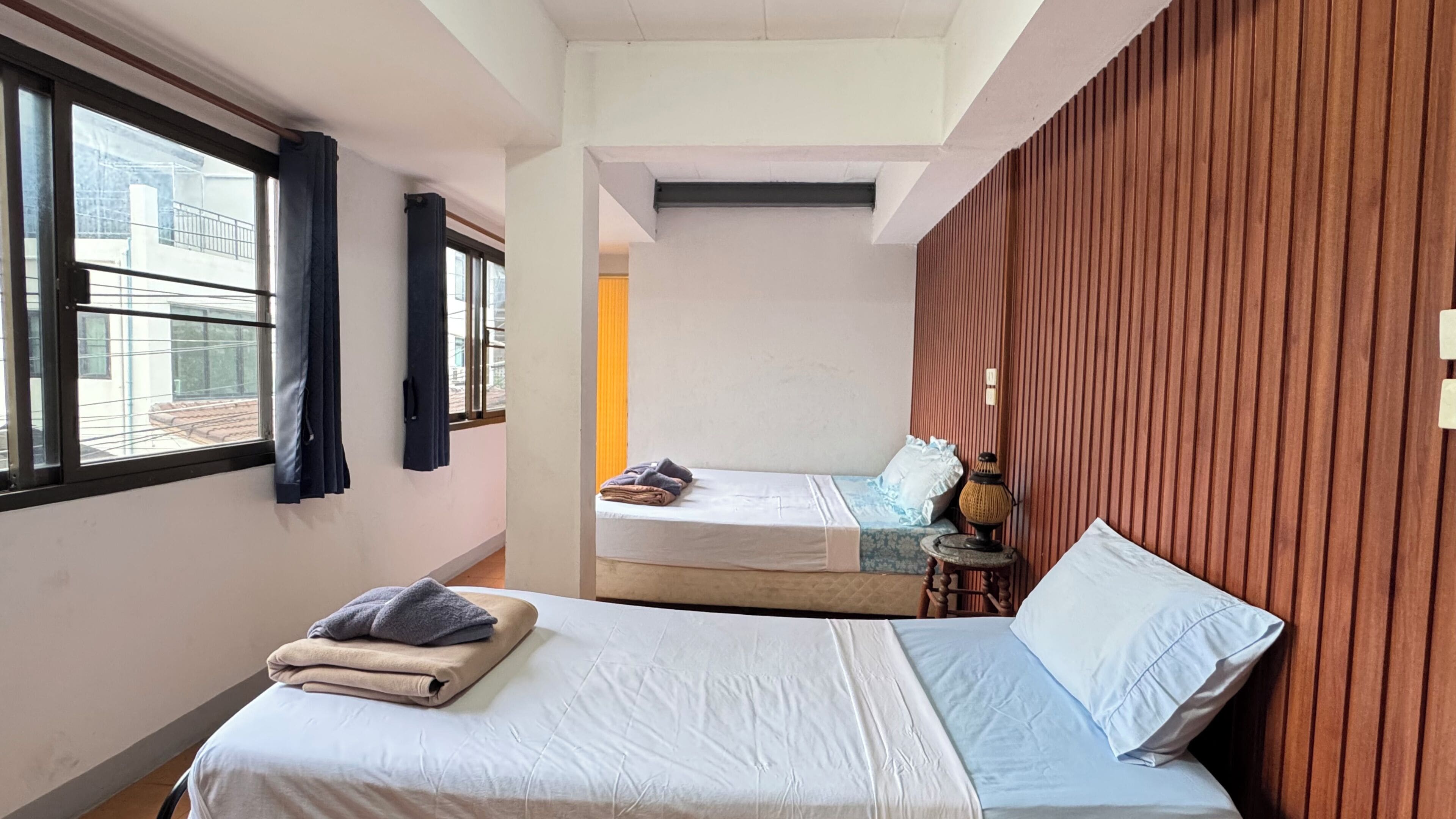 Una habitación pequeña con cama, una cama individual, ventana y lámpara de pared.