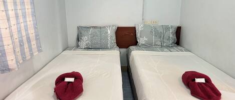 Two single beds with matching headboards and pillows, a window with a grid pattern, and a visible electrical outlet on the wall.
