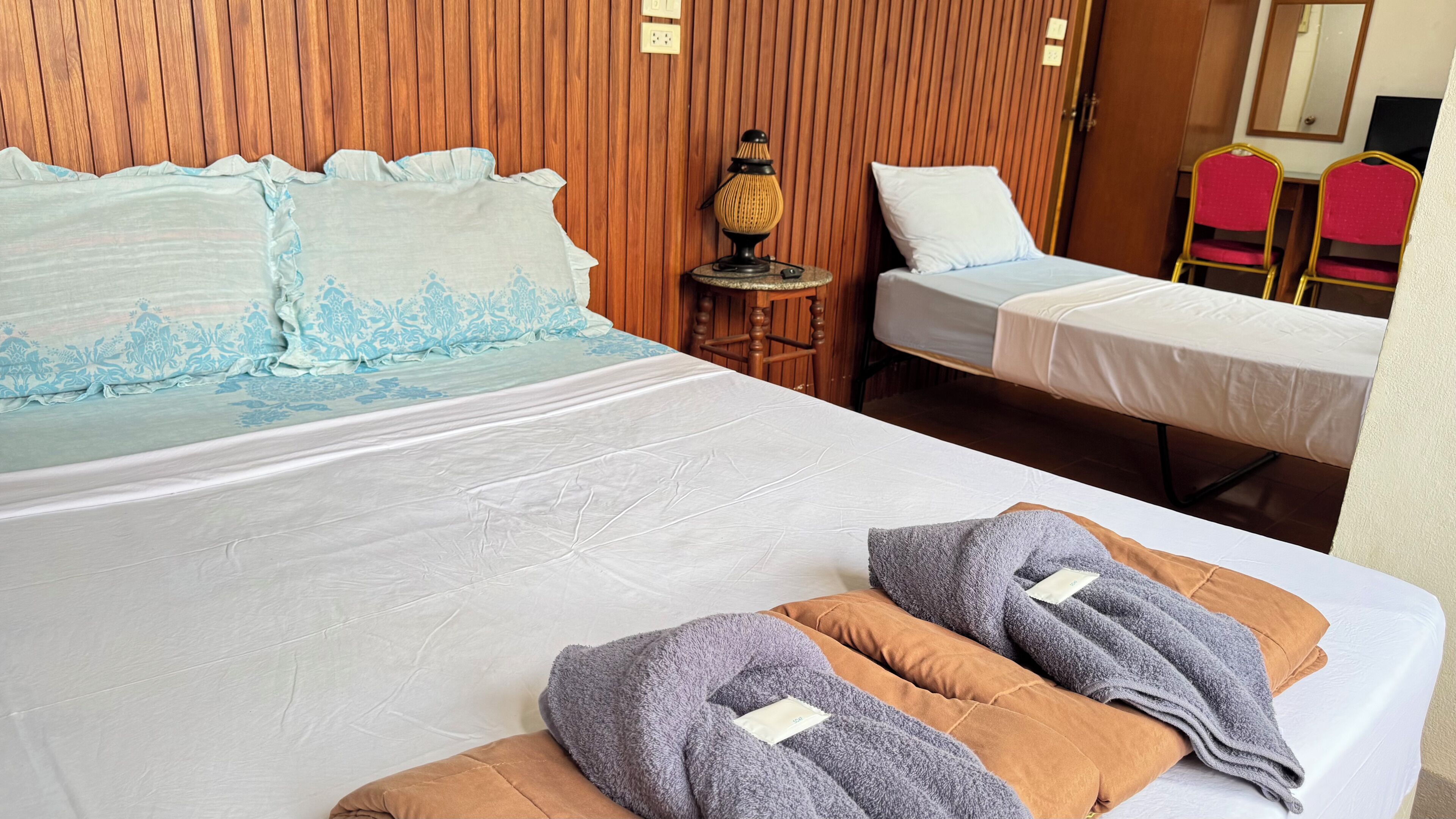 A hotel room with a large bed, a smaller bed, a massage table, and a wooden wall.