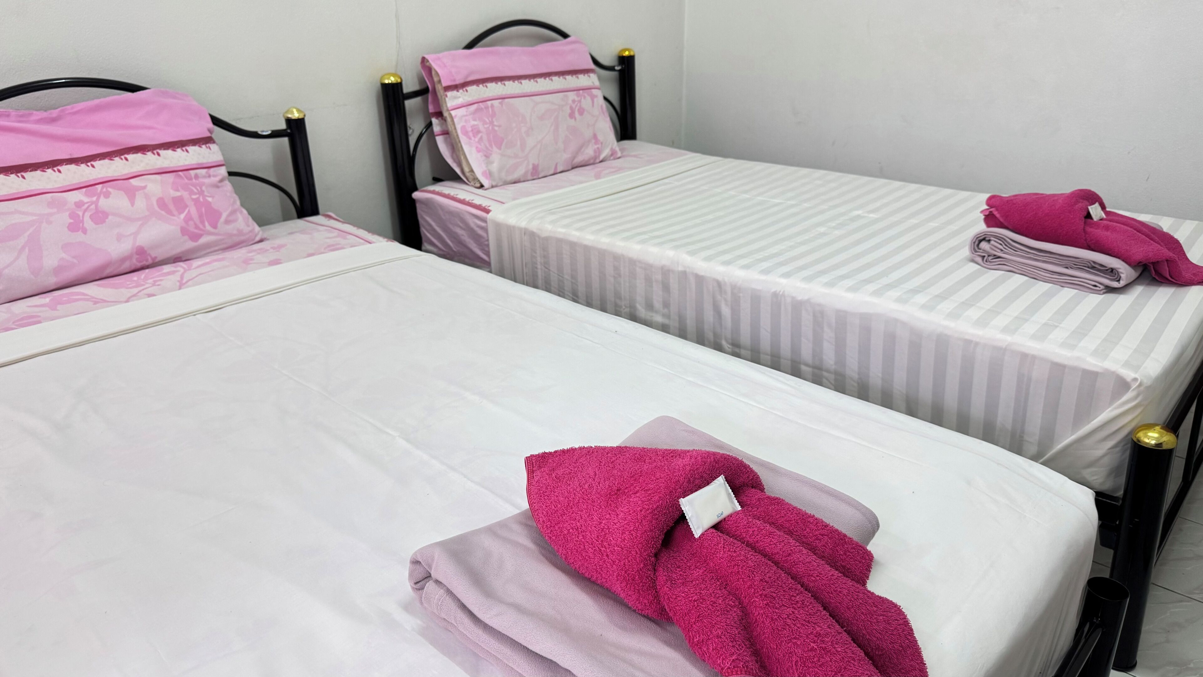 Two single beds with headboards, a folded towel, and a rolled-up towel on the right bed.