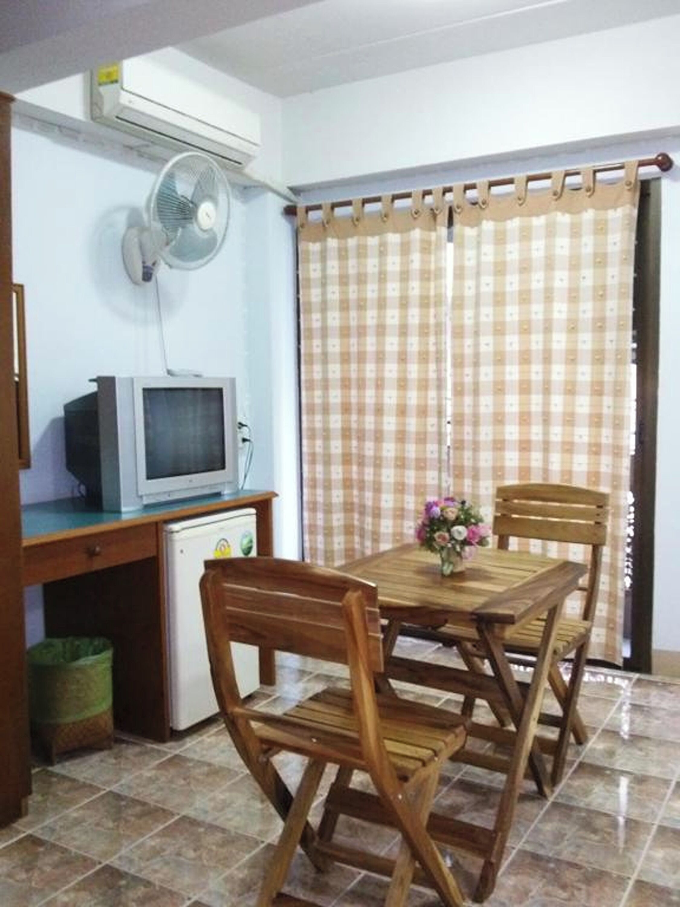 Een eethoek met een houten tafel en stoelen, een kleine koelkast, een televisie en een ventilator.