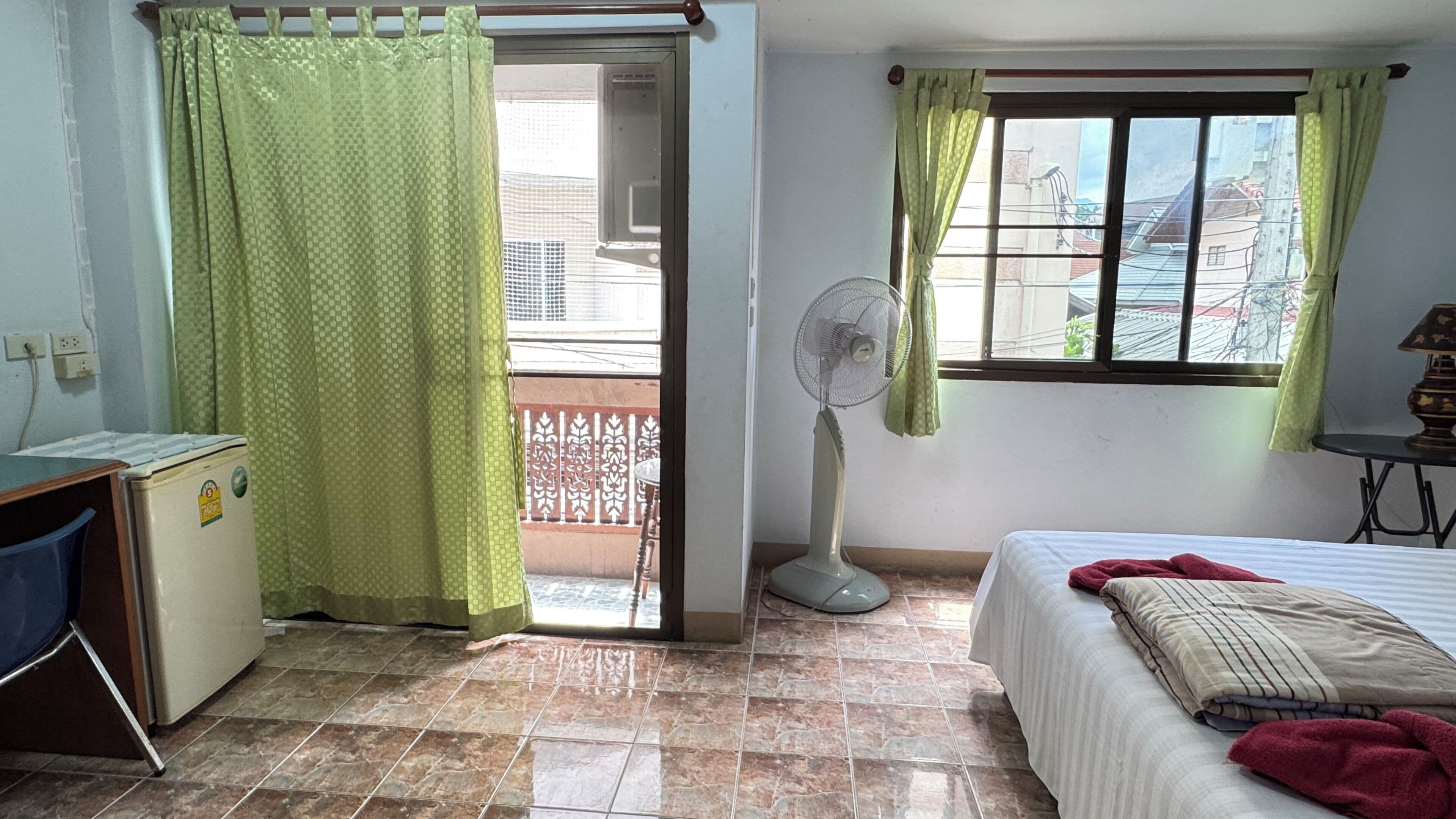 A room with a bed, a desk, a fan, and a window with curtains.