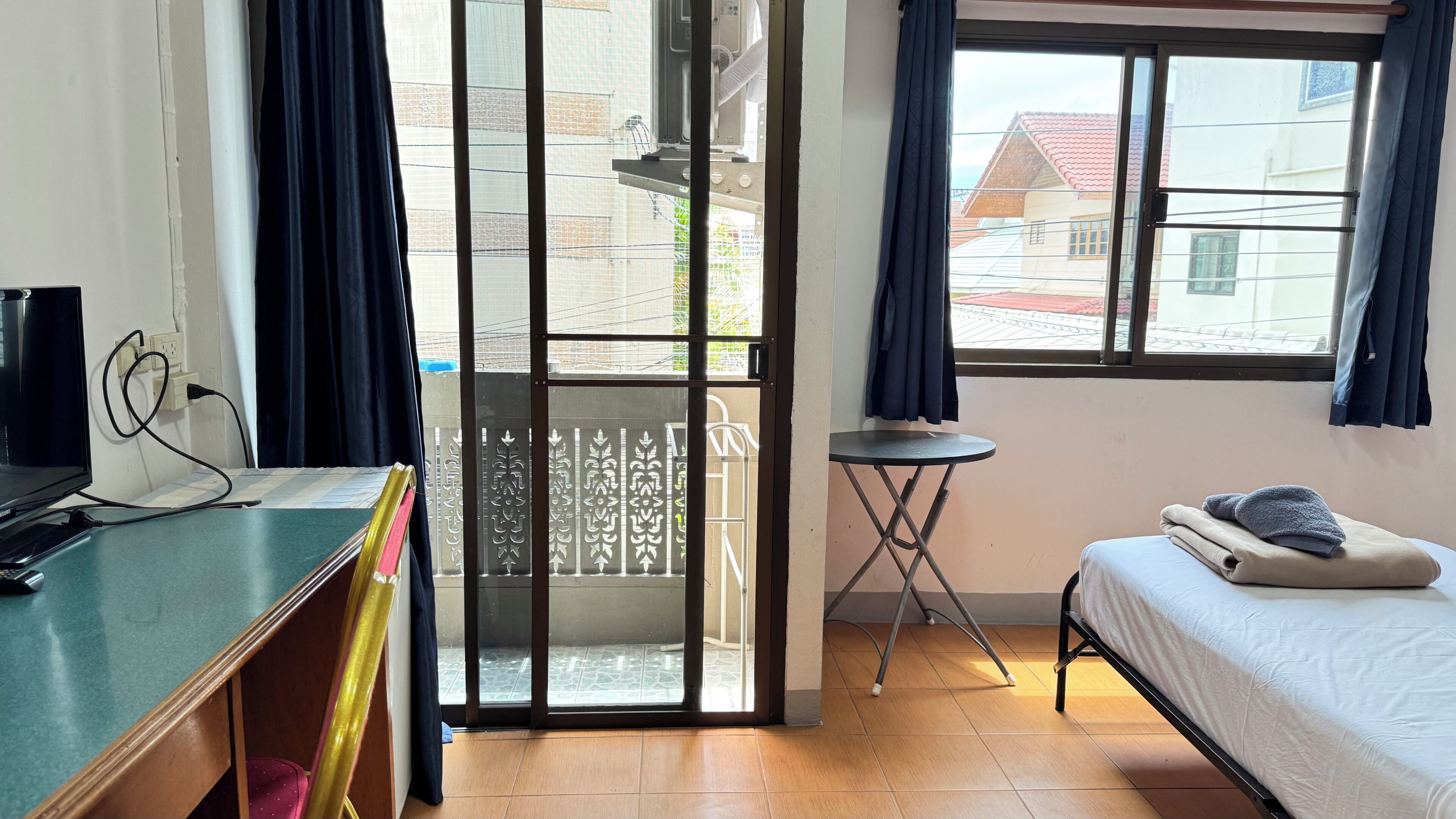 A room with a bed, a desk, a chair, a small table, and a window with curtains.