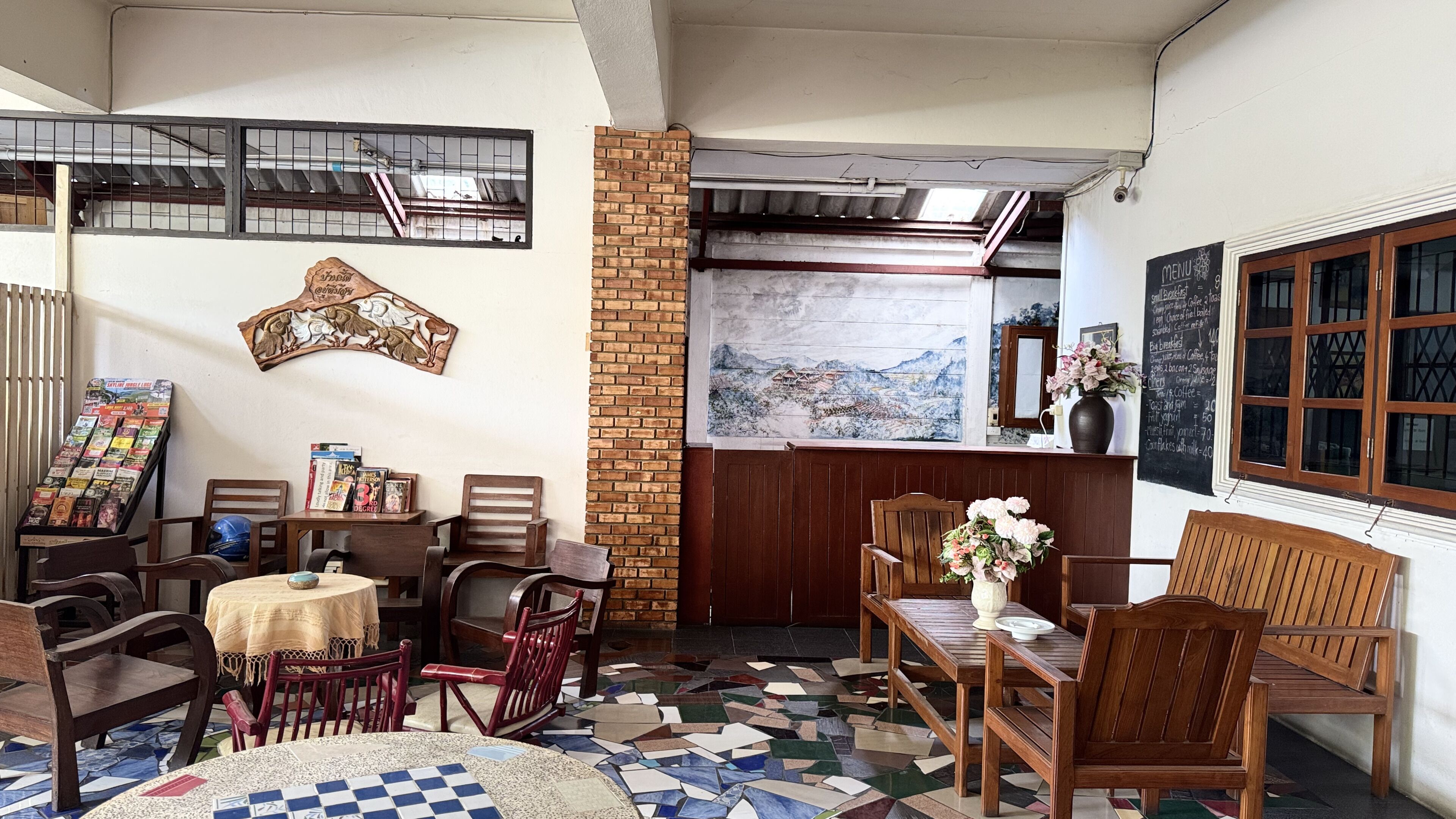 A cozy restaurant interior with a mosaic floor, wooden furniture, a brick column, and a menu board.