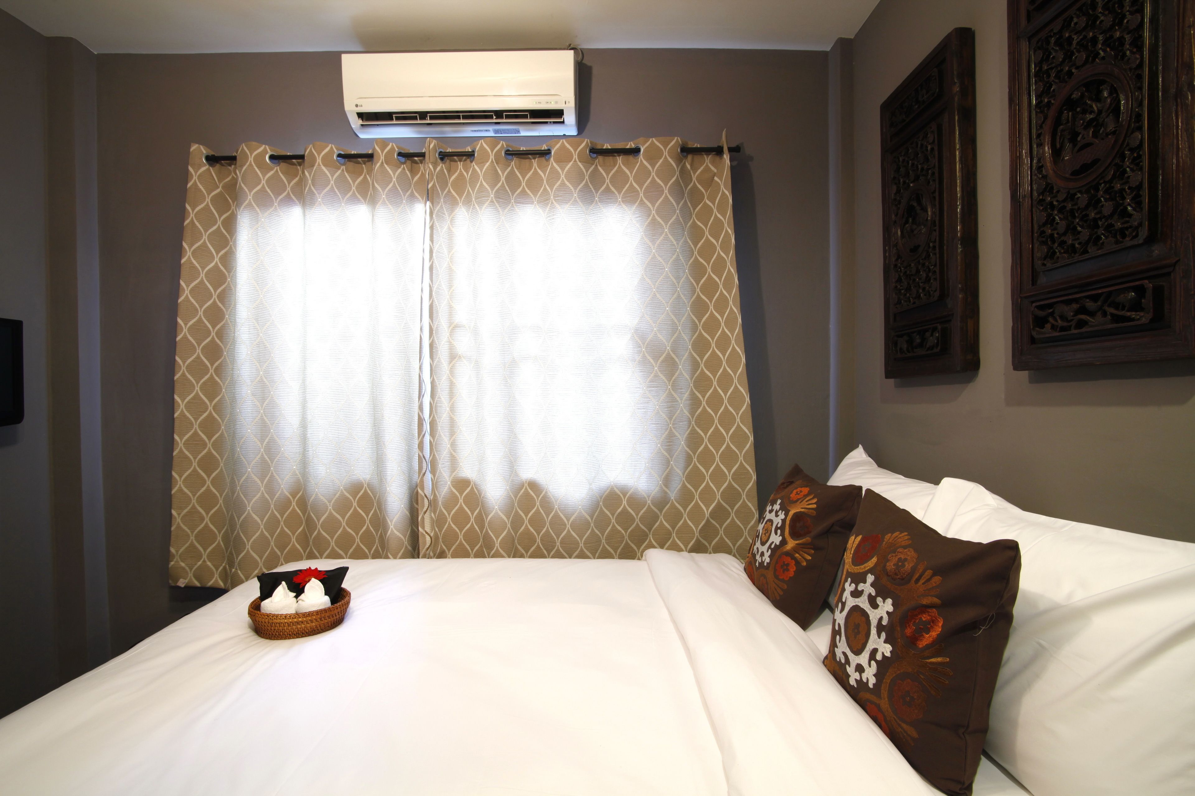 A hotel room with a bed, a decorative wall panel, and a window with curtains.