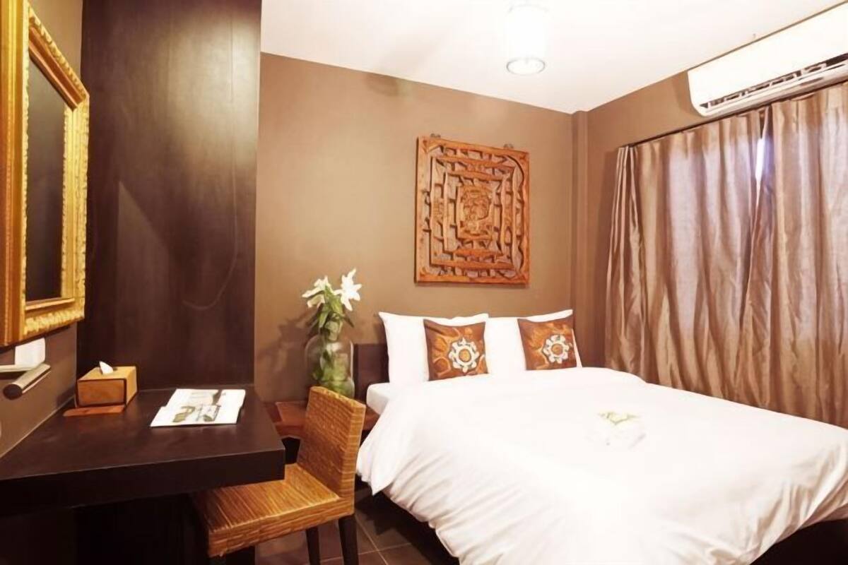 Ein Hotelzimmer mit Bett, Schreibtisch mit Stuhl, Spiegel, Wanddeko und Klimaanlage.