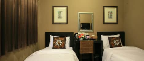 Une chambre d’hôtel avec deux lits simples, un bureau avec une chaise, un miroir et des tableaux encadrés aux murs.