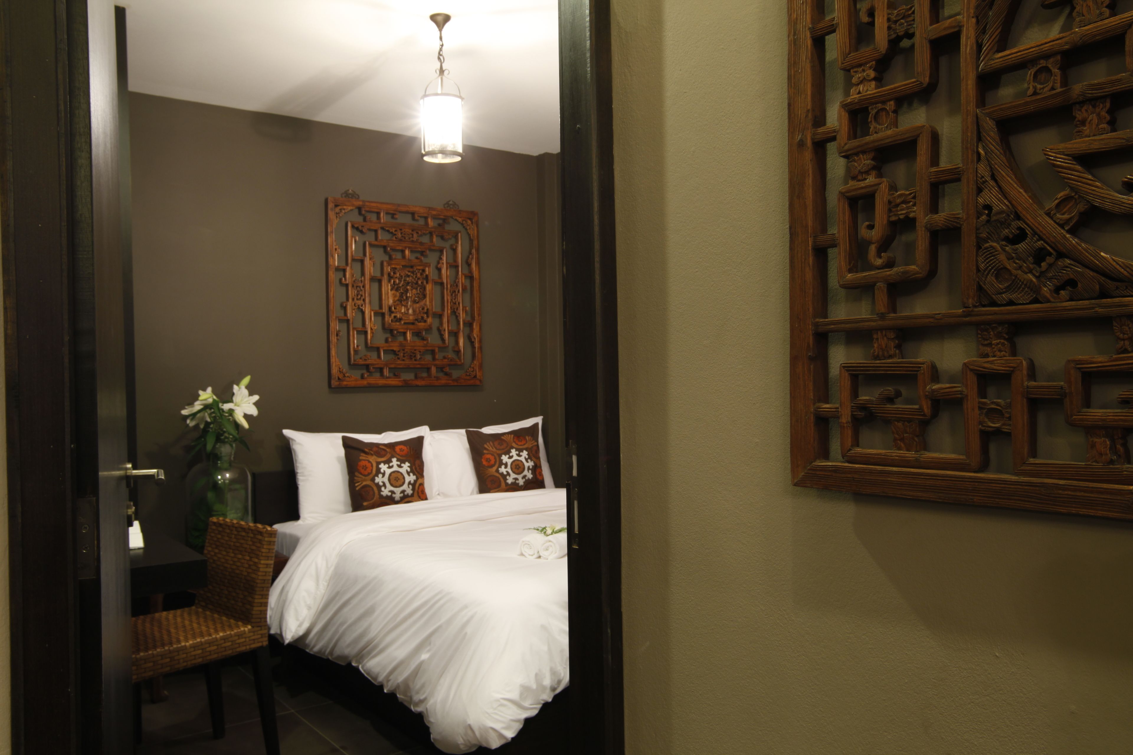 A hotel room with a bed, a chair, a vase with flowers, and a decorative wall piece.