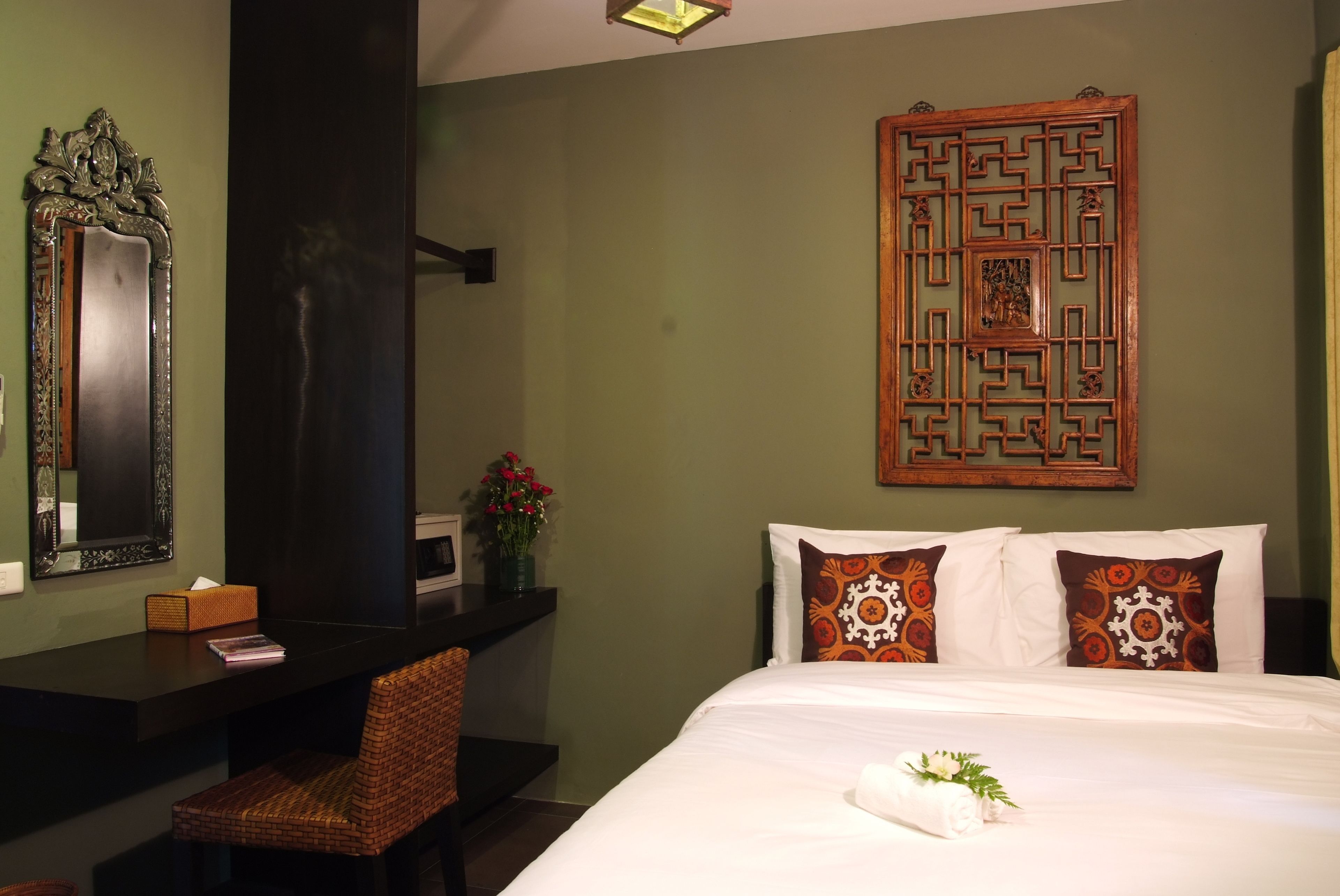 A hotel room with a bed, a desk with a chair, a mirror, and a decorative wall piece.