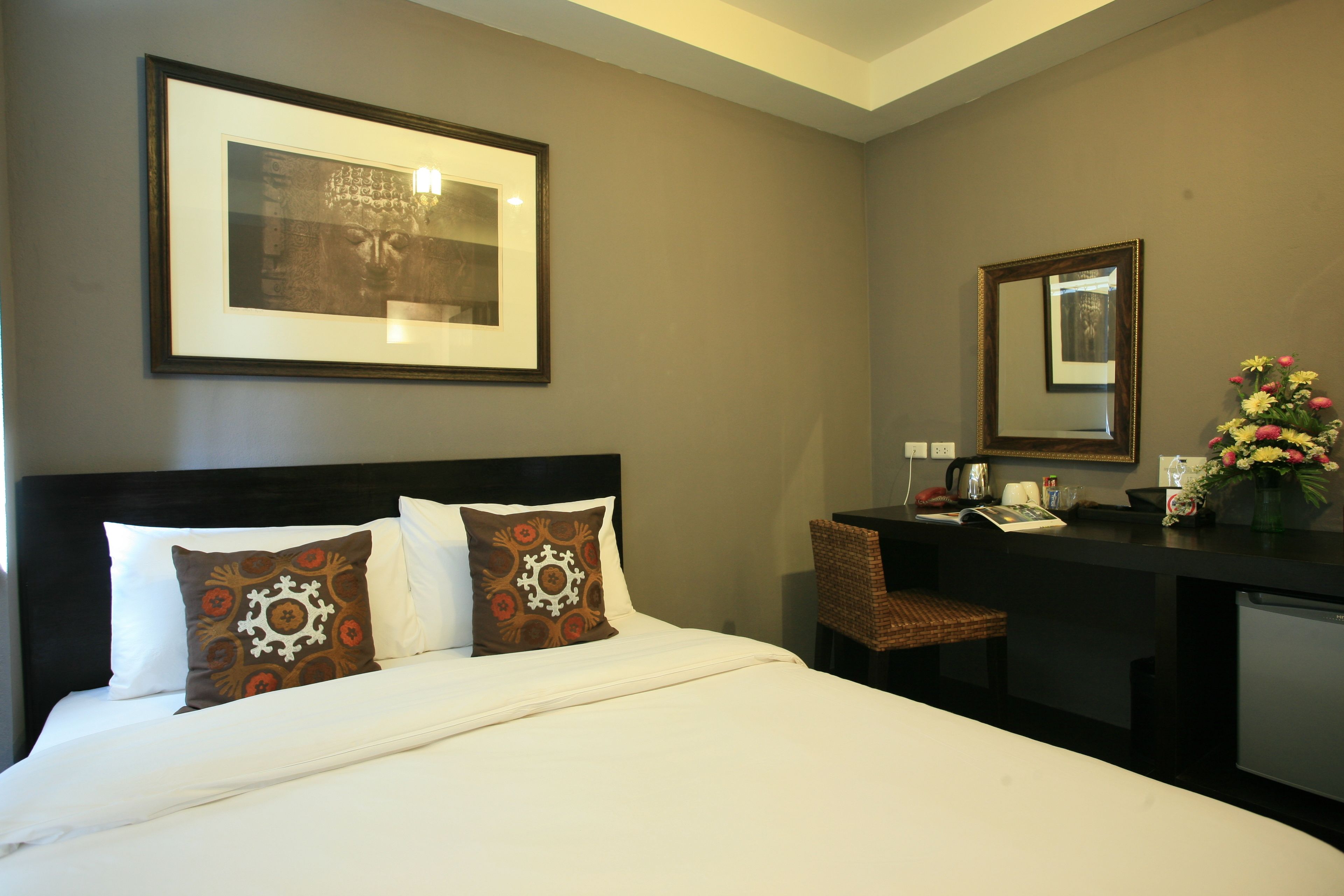 A hotel room with a bed, a desk, a chair, a mirror, and a framed picture on the wall.