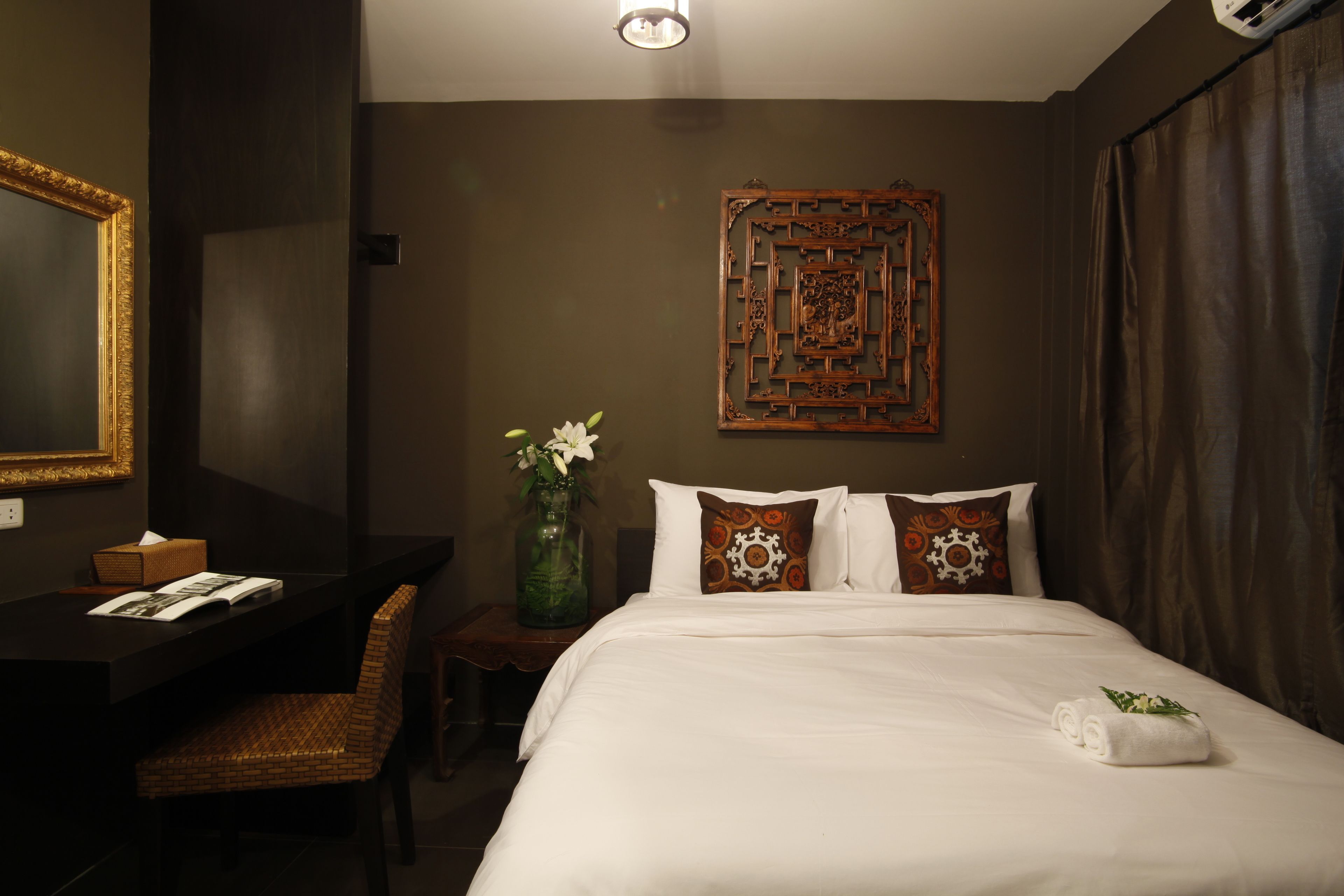 Habitación de hotel con cama, escritorio, silla, un florero con flores y un adorno en la pared.