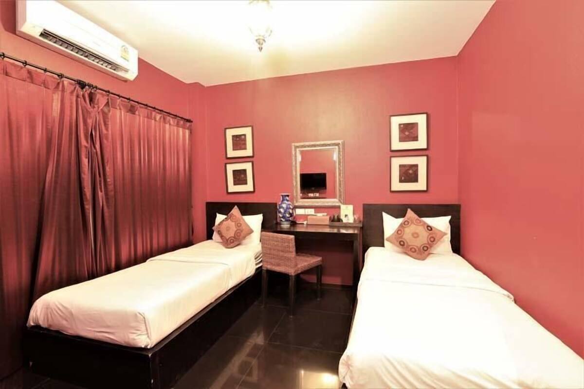 Ein Hotelzimmer mit zwei Einzelbetten, einem Schreibtisch mit Stuhl, einem Spiegel und einer Wandklimaanlage.