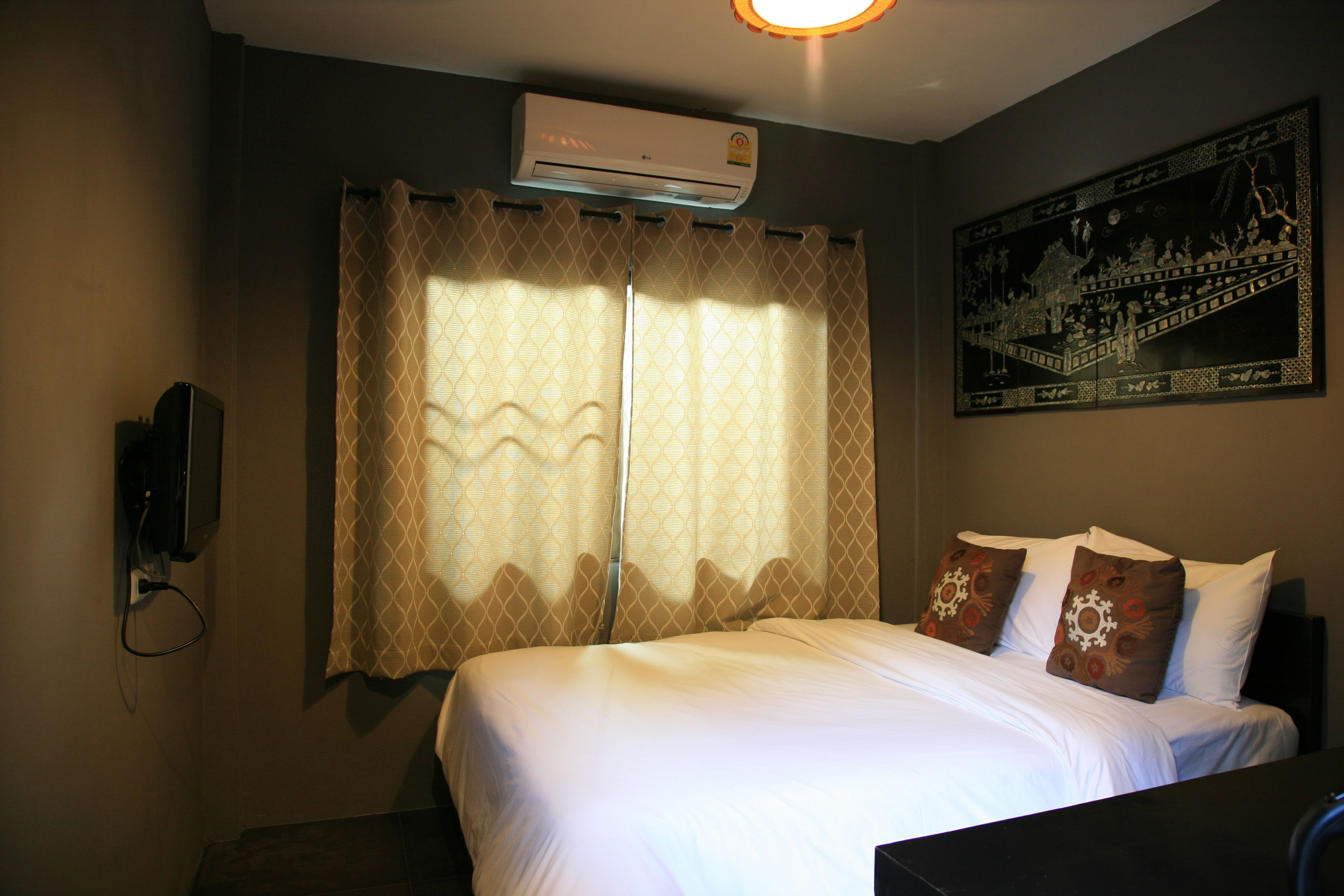 Habitación de hotel con cama, cortinas, aire acondicionado, un cuadro en la pared y un teléfono en la pared.