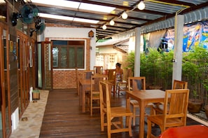 A wooden-floored patio with tables and chairs, a brick wall, and a bamboo fence. - Swiss Lanna Lodge (Chiang Mai)