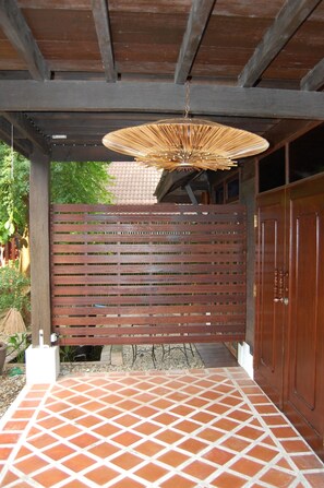 A covered patio area with a tiled floor, a wooden fence, and a hanging light fixture. - Swiss Lanna Lodge (Chiang Mai)