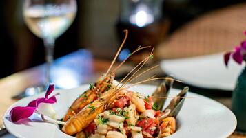 A plate of seafood with a glass of white wine and a vase with purple flowers on the table.