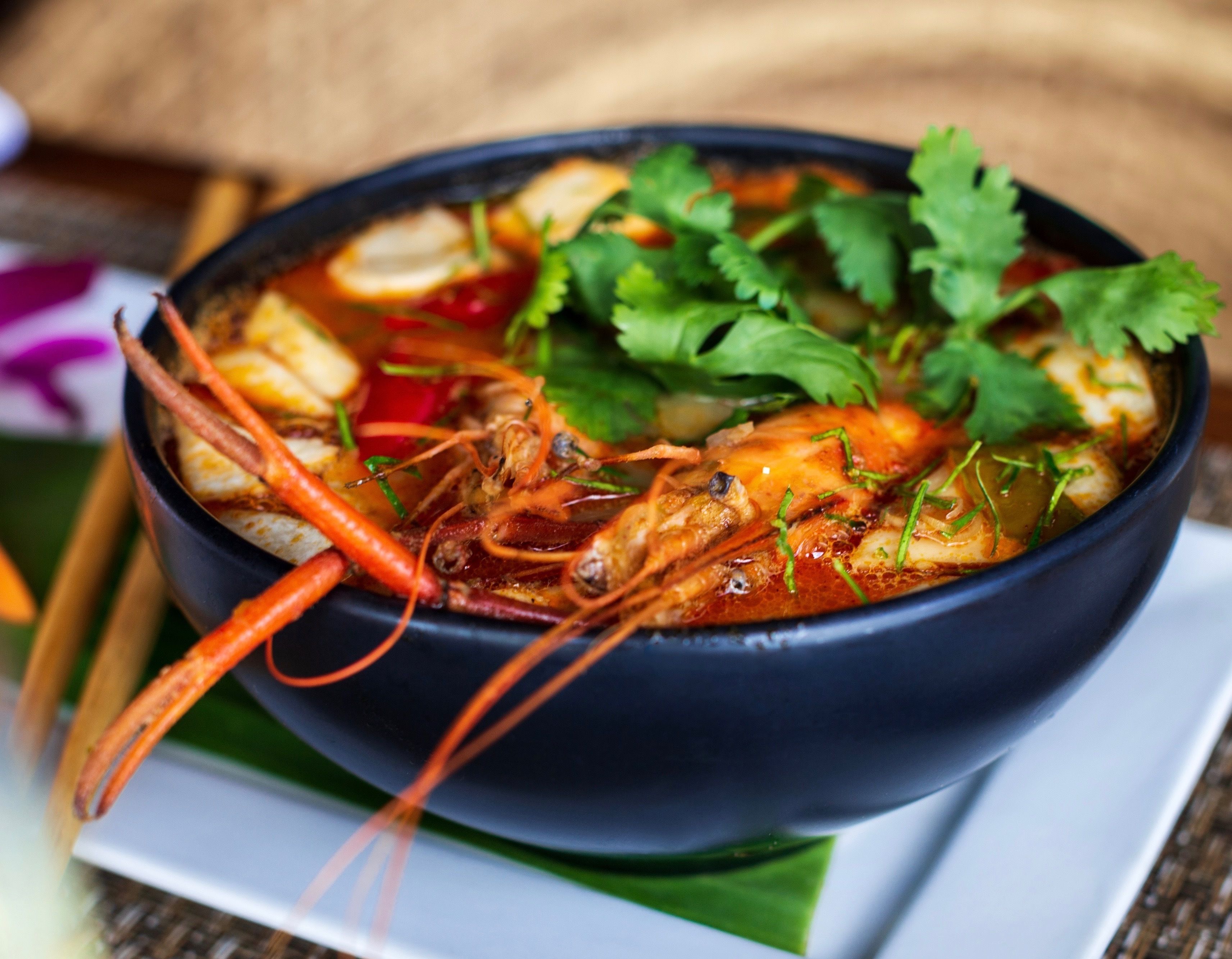 A bowl of soup with shrimp, vegetables, and herbs.