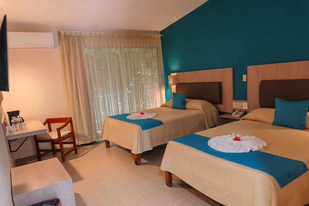 A hotel room with two beds, a desk, a chair, and a trash bin.
