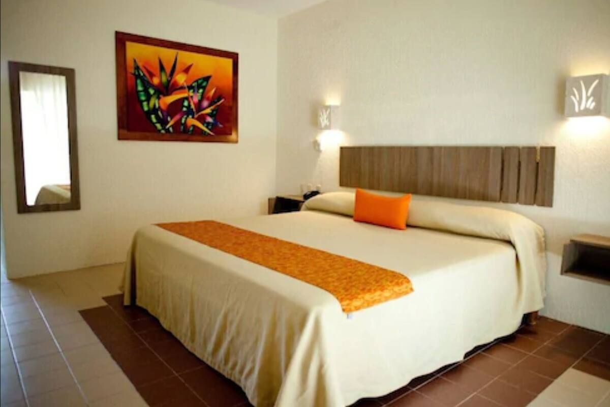 A hotel room with a large bed, a painting on the wall, and two wall-mounted lights.