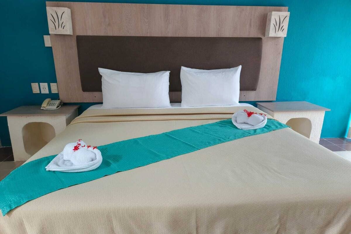 A hotel room with a bed, two pillows, a green towel, and a folded towel on the bed.