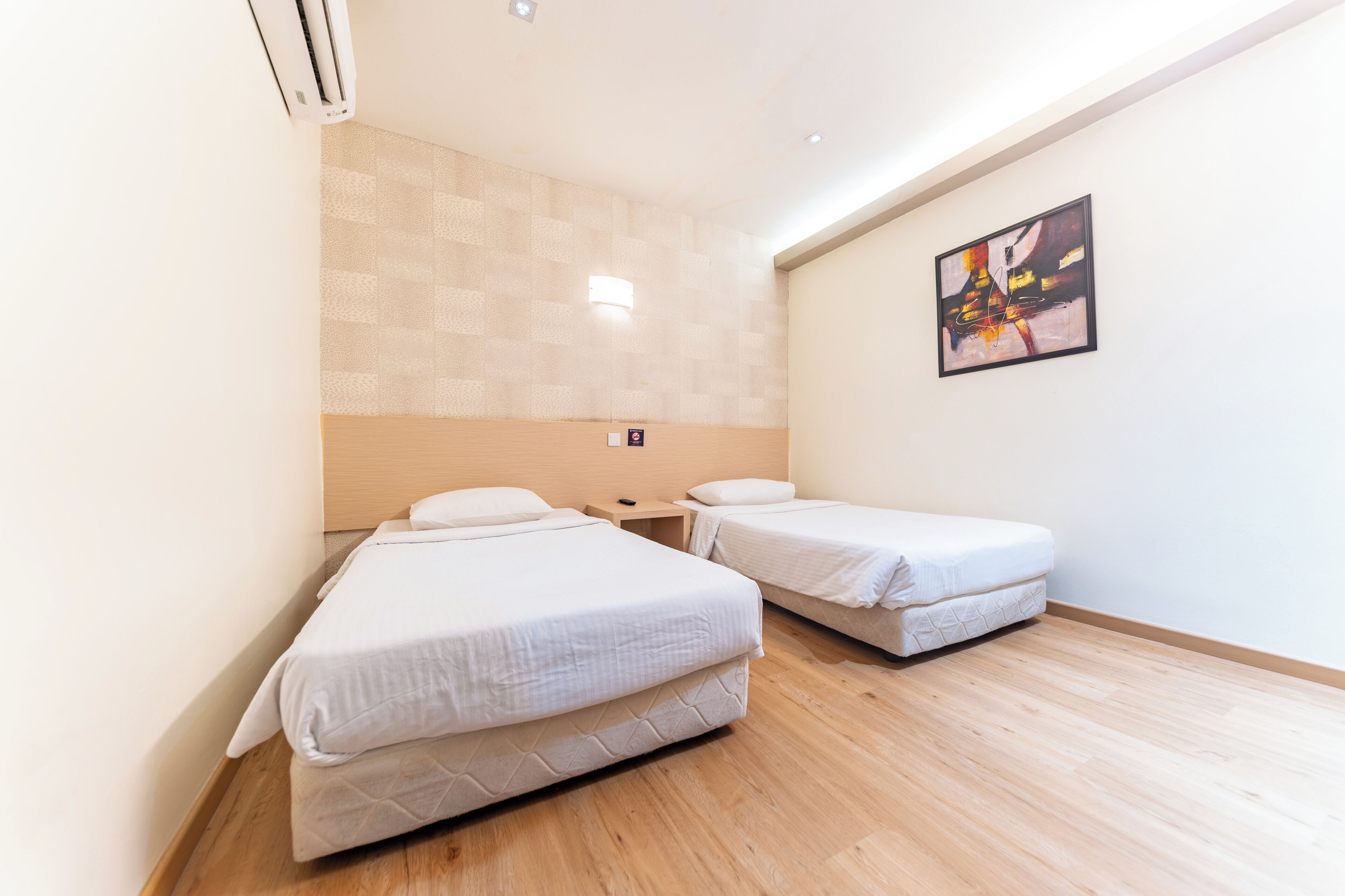 Habitación de hotel con dos camas, suelo de madera, aire acondicionado instalado en la pared, una mesita y un cuadro.