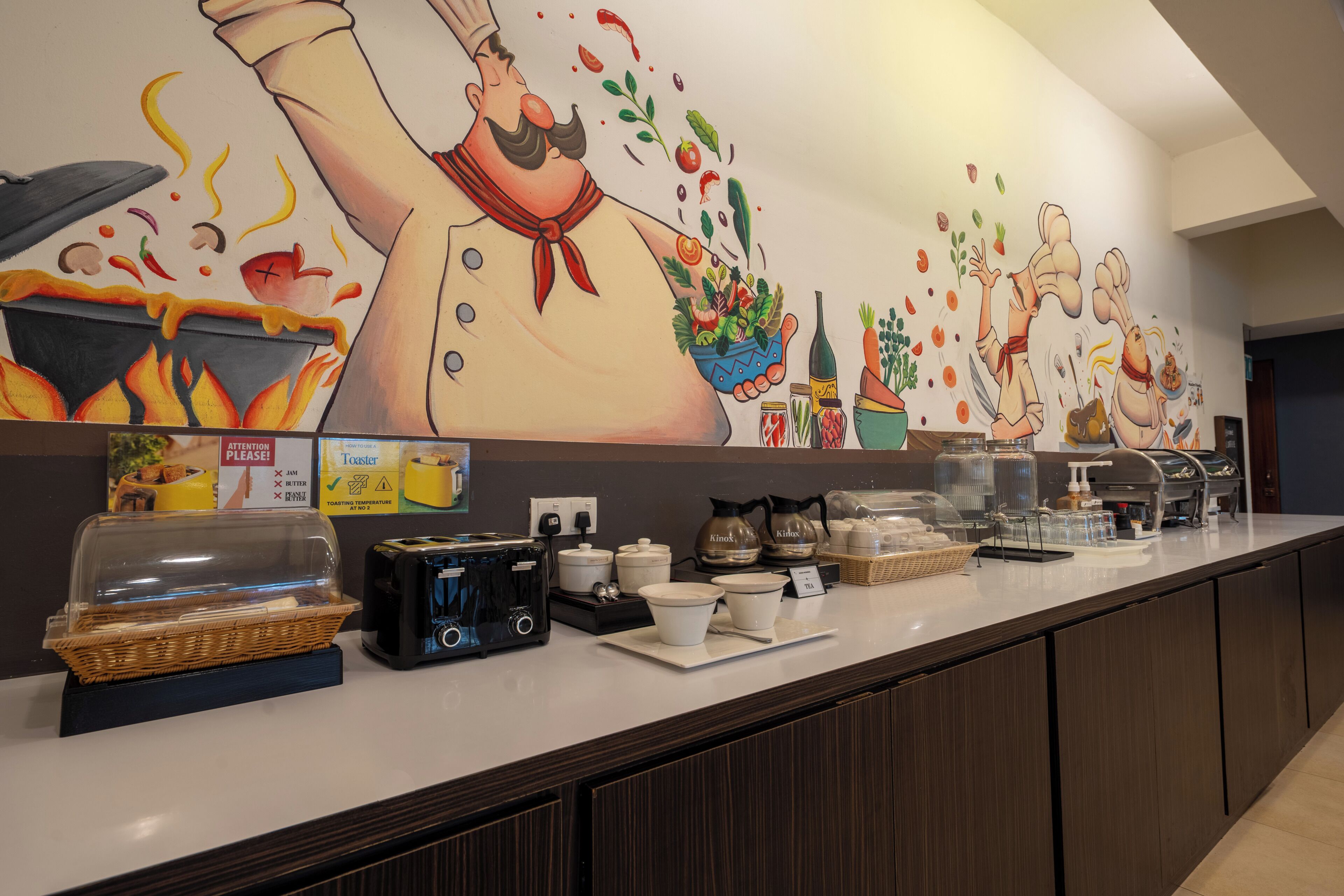Un espace buffet agrémenté d’une grande fresque murale, d’un grille-pain et de différents récipients pour les aliments.