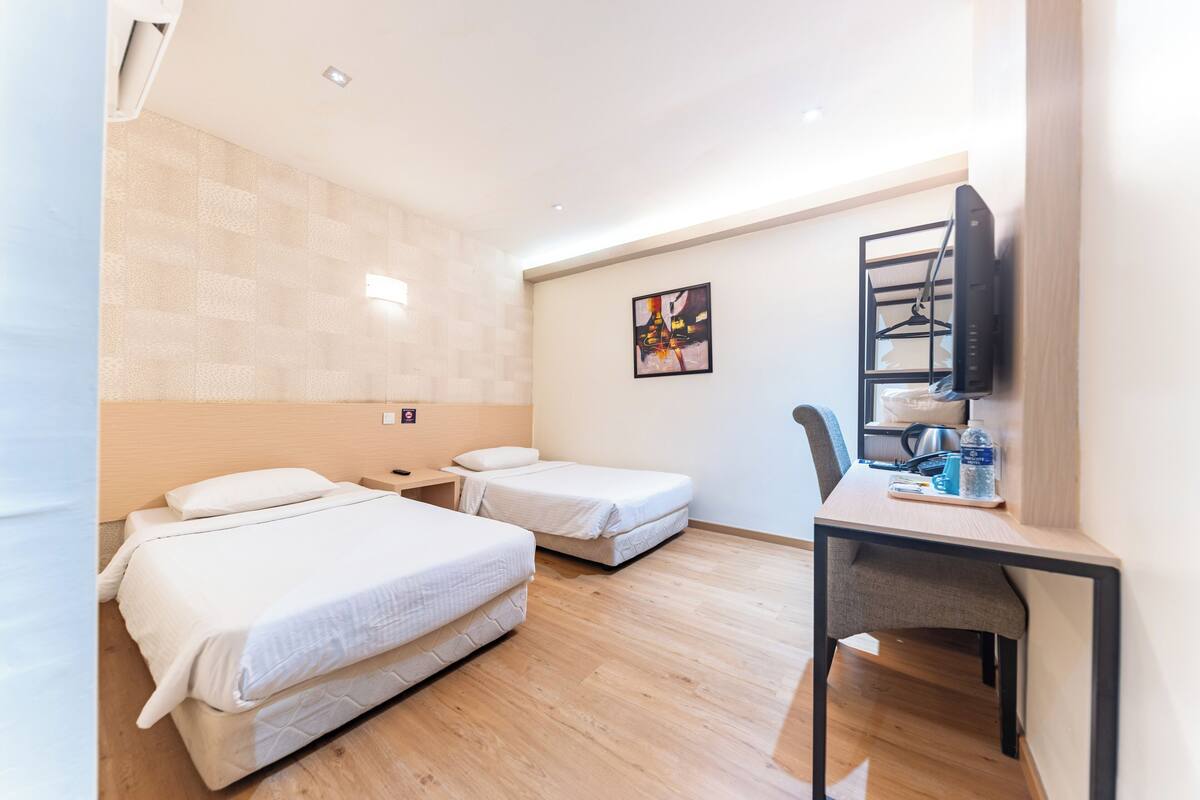 Une chambre d’hôtel avec deux lits, un bureau avec une chaise, un téléviseur fixé au mur et un tableau.