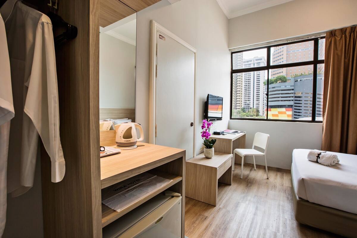 A hotel room with a bed, a desk, a chair, a wardrobe, and a window with a city view.