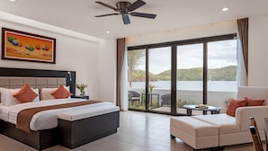 A modern hotel room with a large bed, a sofa, a ceiling fan, and a view of a lake. - Busuanga Bay Lodge (Busuanga)