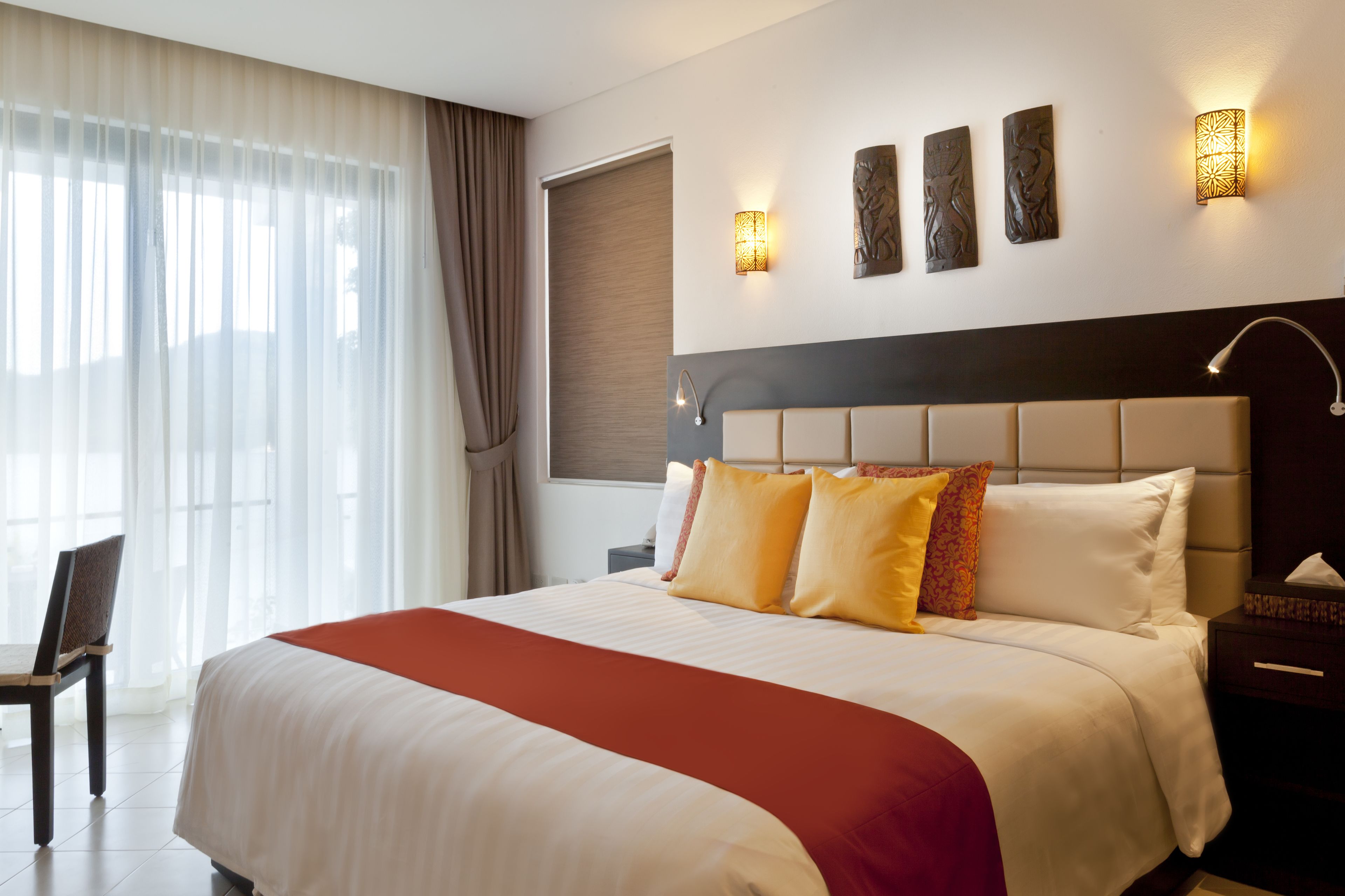 A hotel room with a large bed, a nightstand, a chair, and a window with curtains.