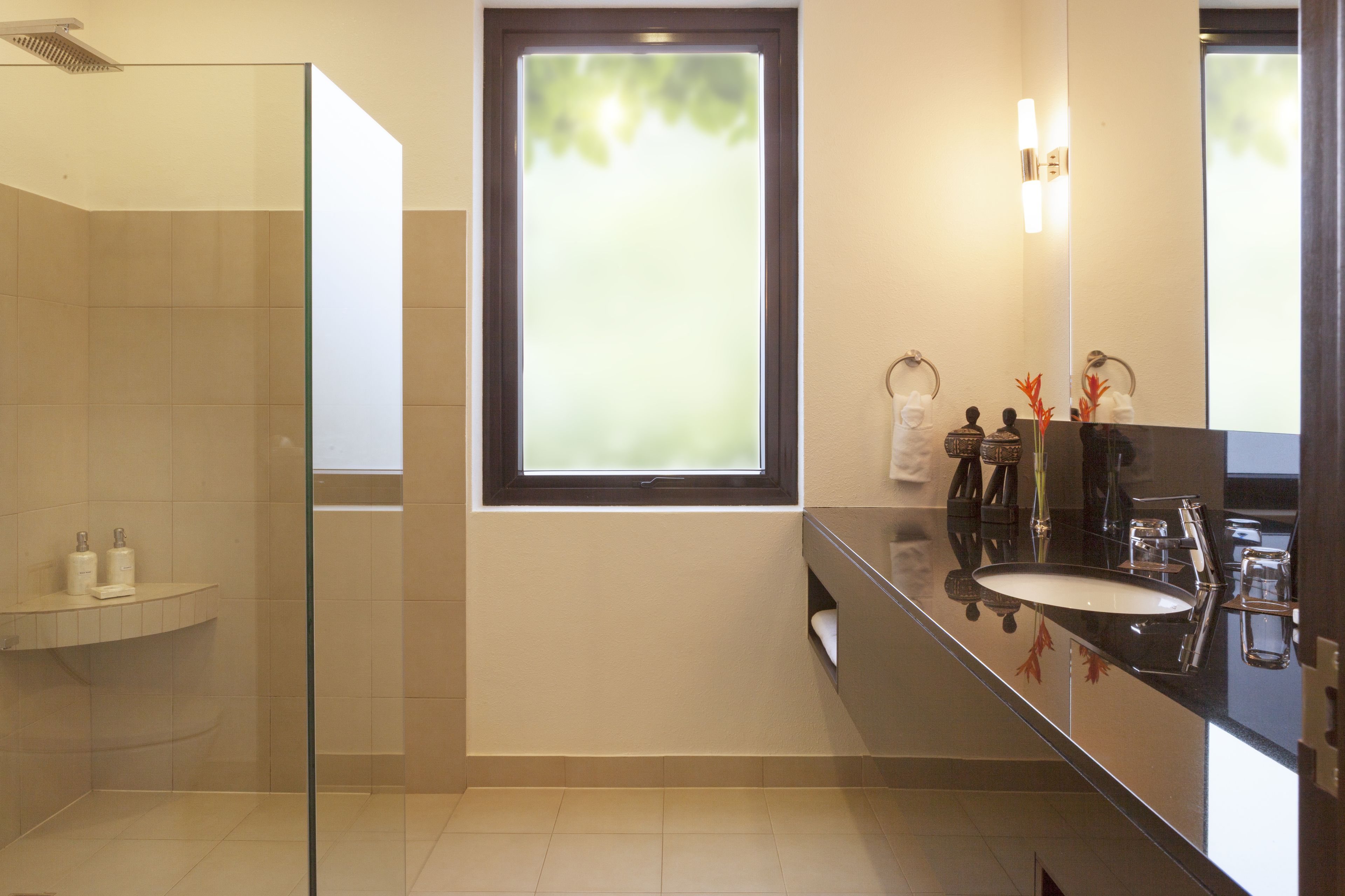 Un bagno moderno con cabina doccia in vetro, un'ampia finestra e un lavabo con specchio su un piano d'appoggio nero.