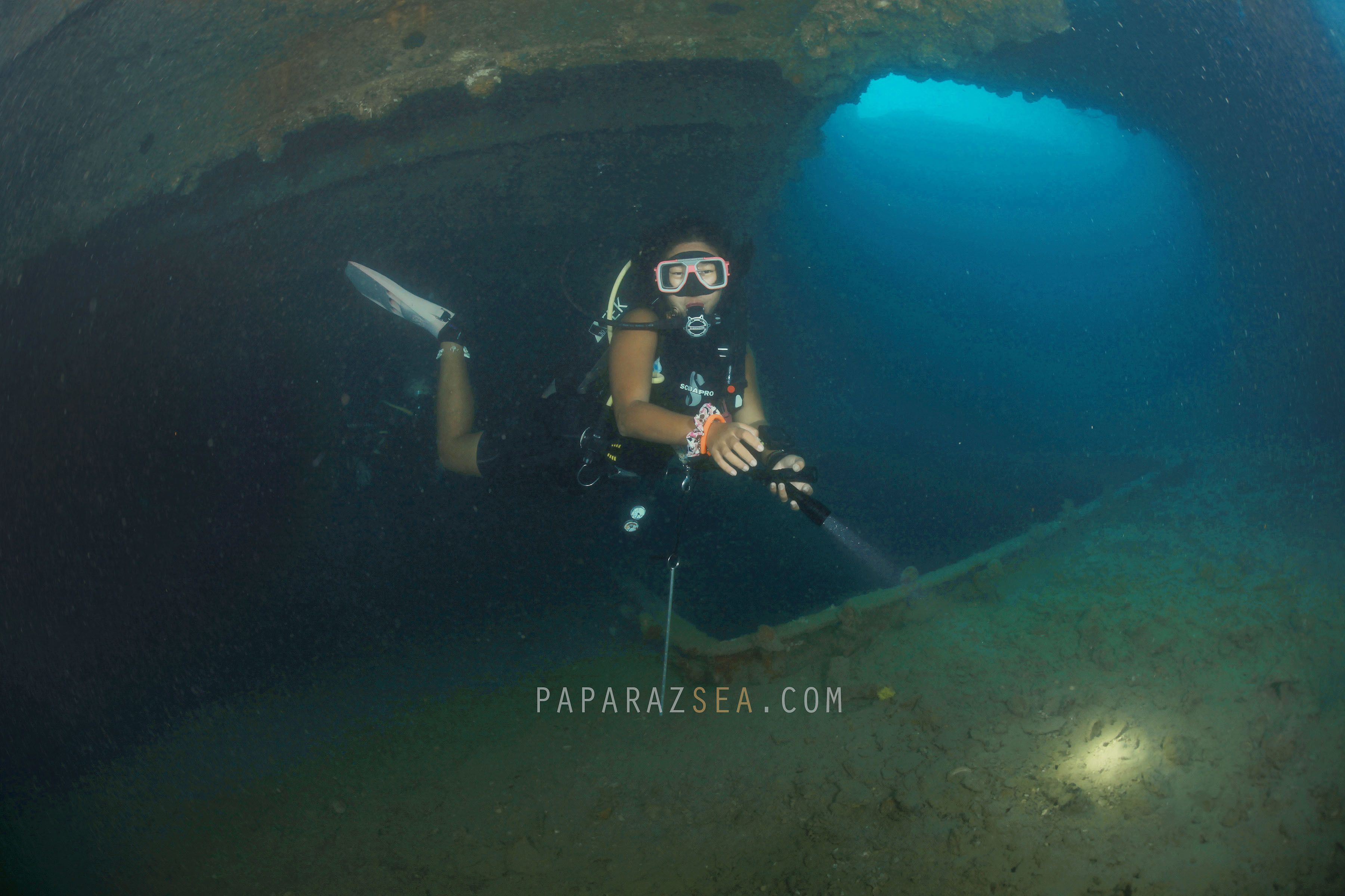 Un buceador bajo el agua en una cueva, con una linterna y una cámara.