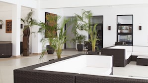 A spacious lobby with high ceilings, large windows, and a central seating area with a white sofa and a dark wicker bench. - Busuanga Bay Lodge (Busuanga)